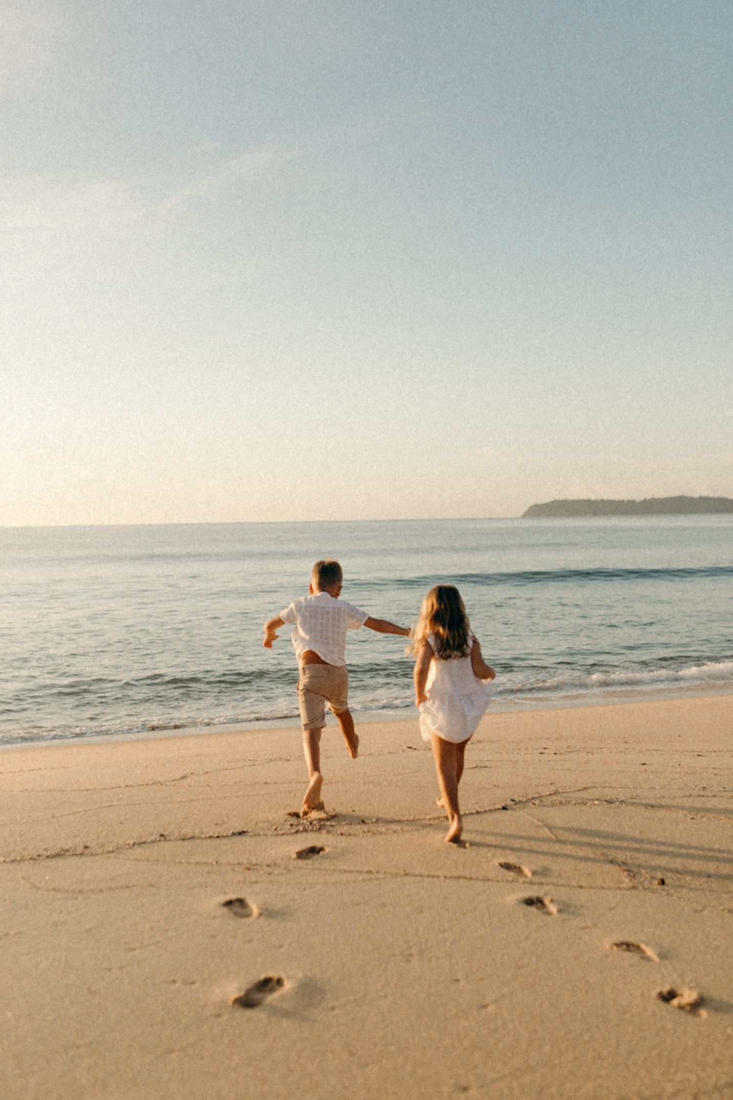 Couple running together on empty beach at sunset leaving footprints in sand.