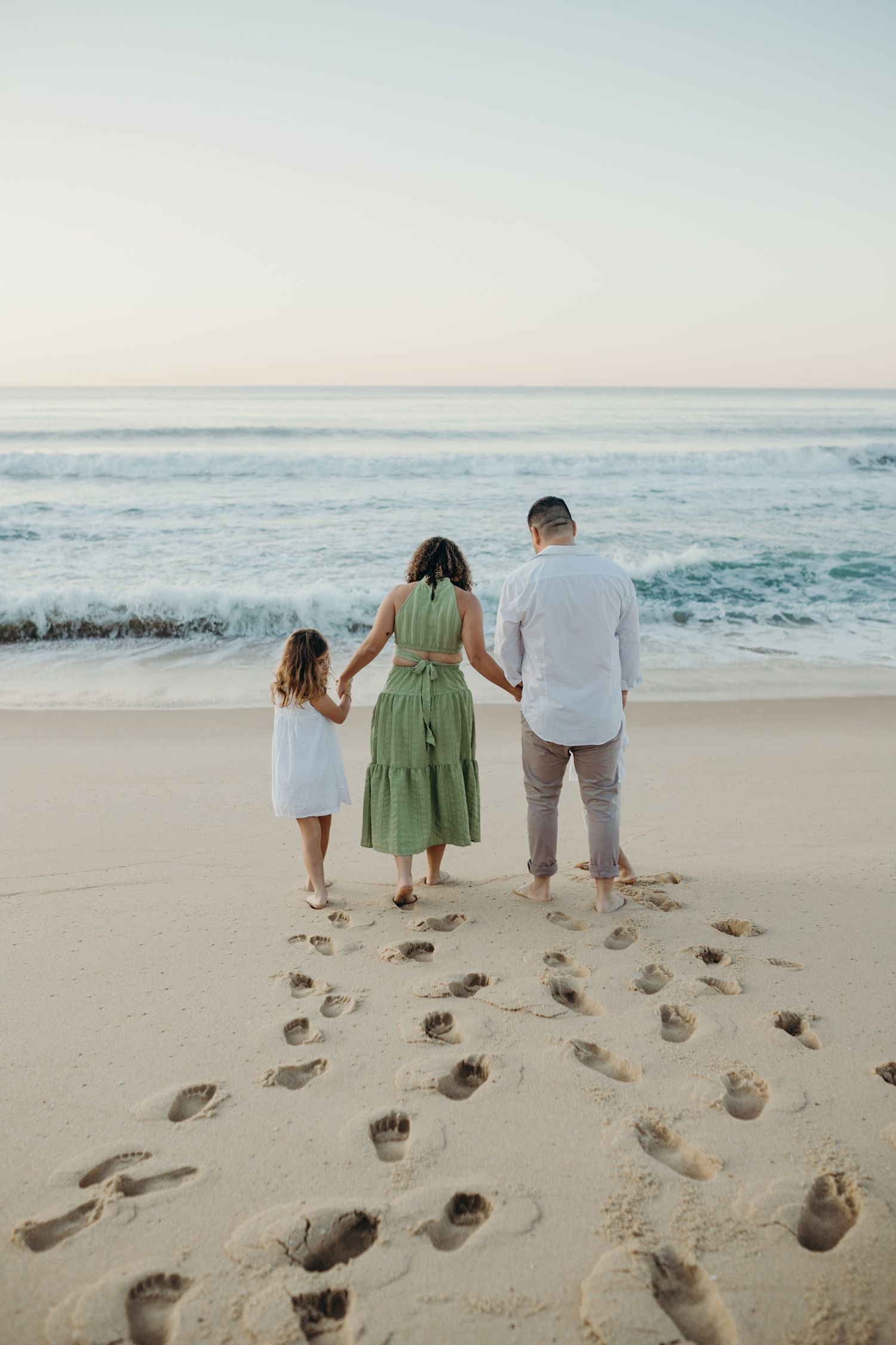Family's footprints trail behind them as they walk along empty beach at dusk.