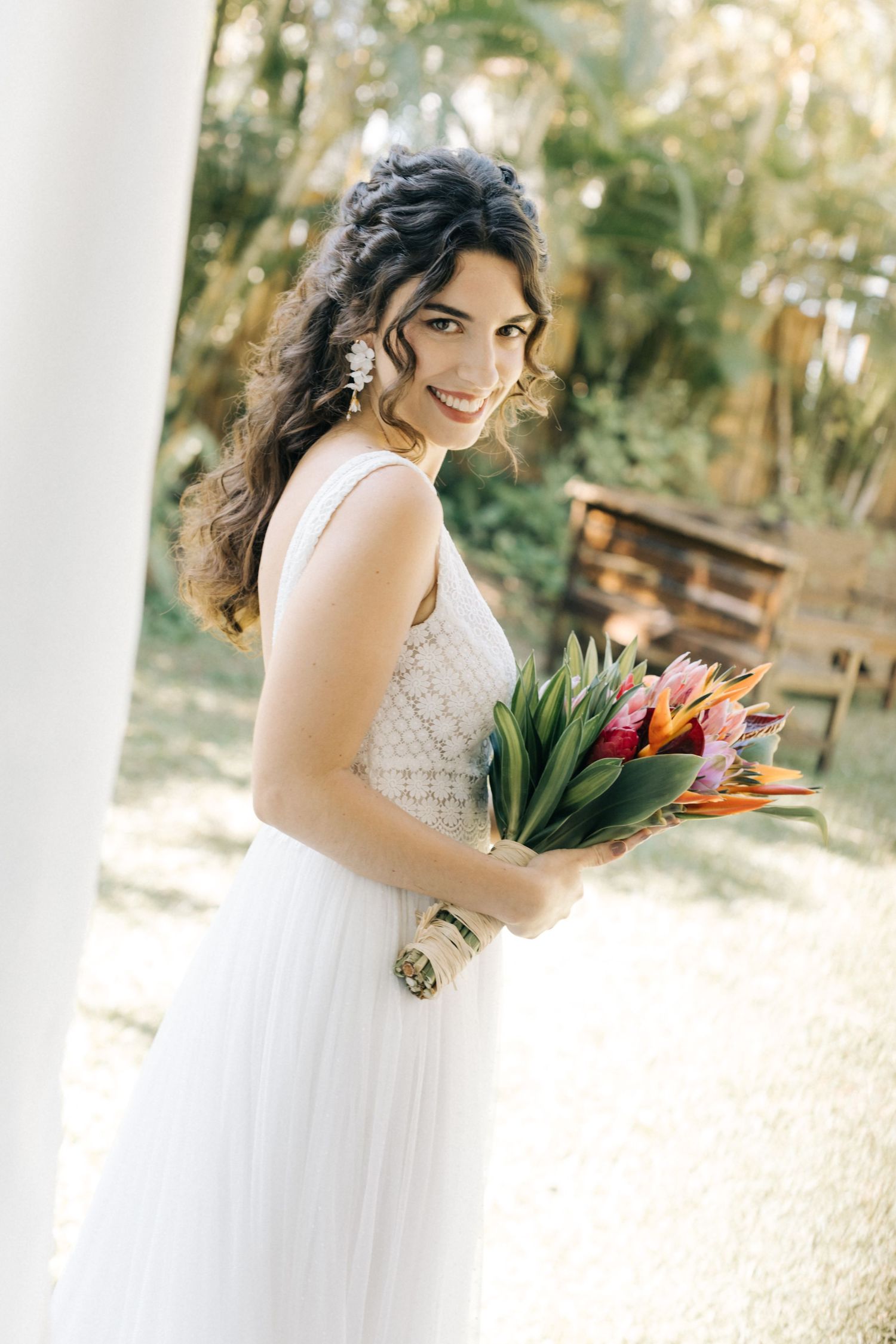 A bride in a white lace dress holding colorful tulips at an outdoor venue.