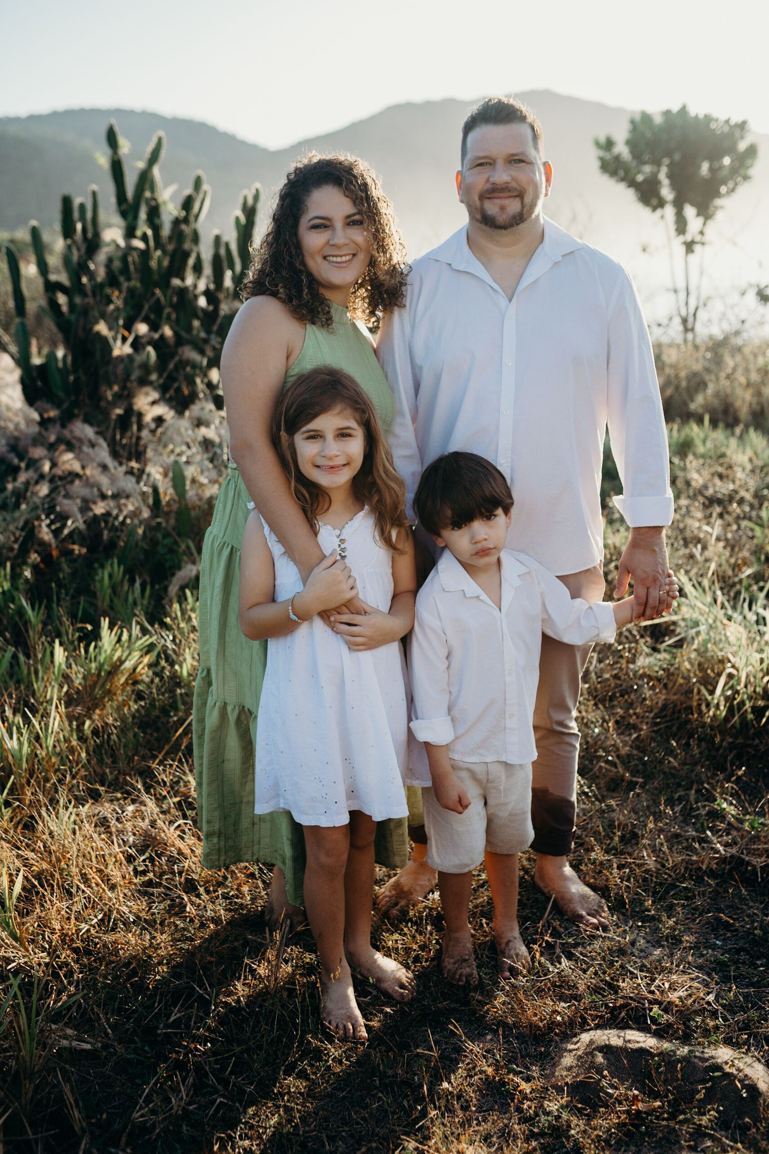 A family of four poses together on a hilltop with mountains and vegetation in the background.