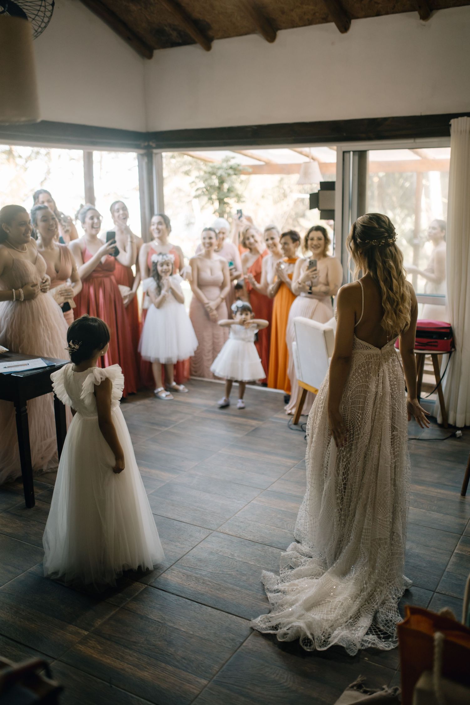 Bridesmaids in blush and coral dresses gather to watch a special moment during a wedding celebration.
