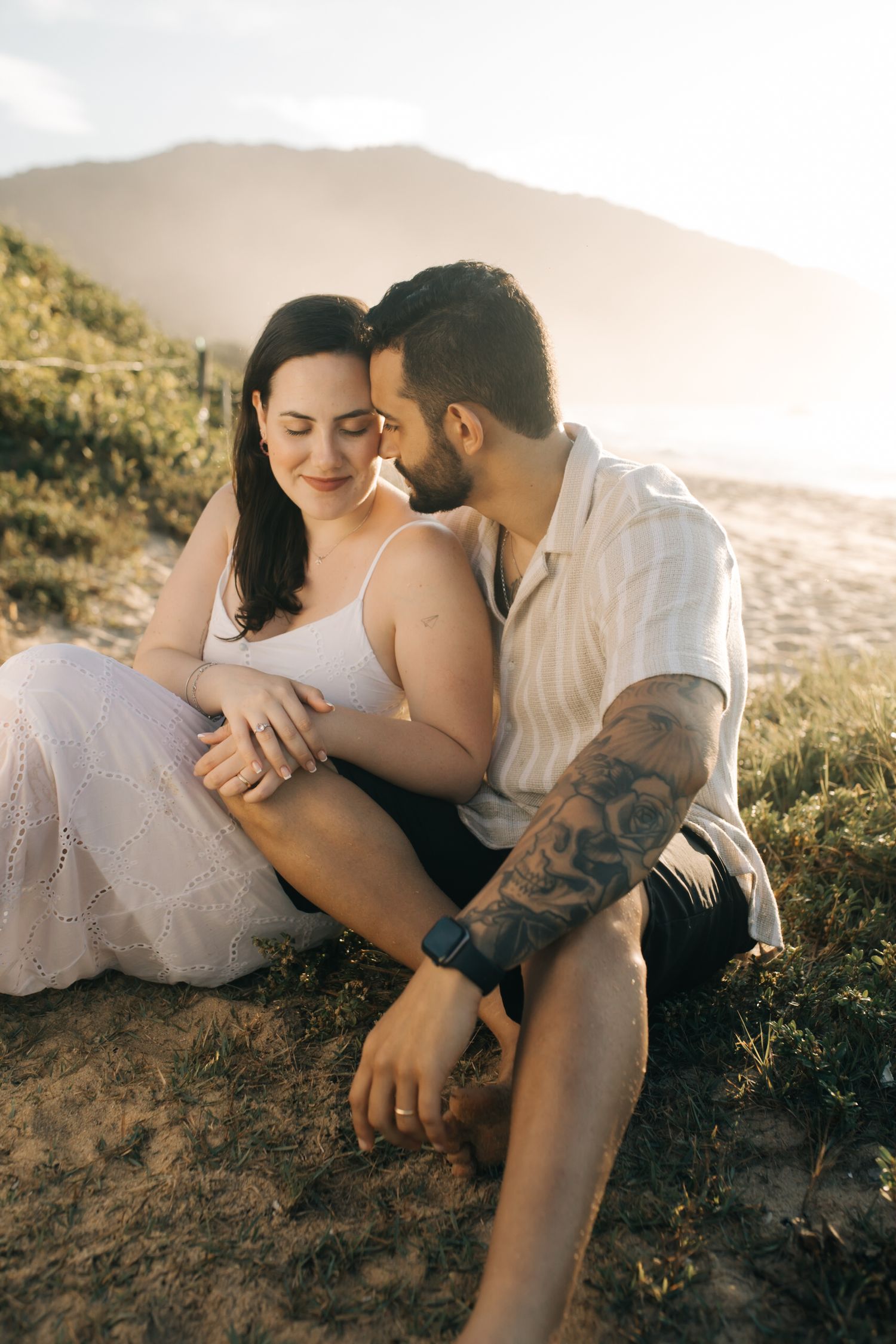 Couple embracing on grassy coastal hillside during sunset photography session.