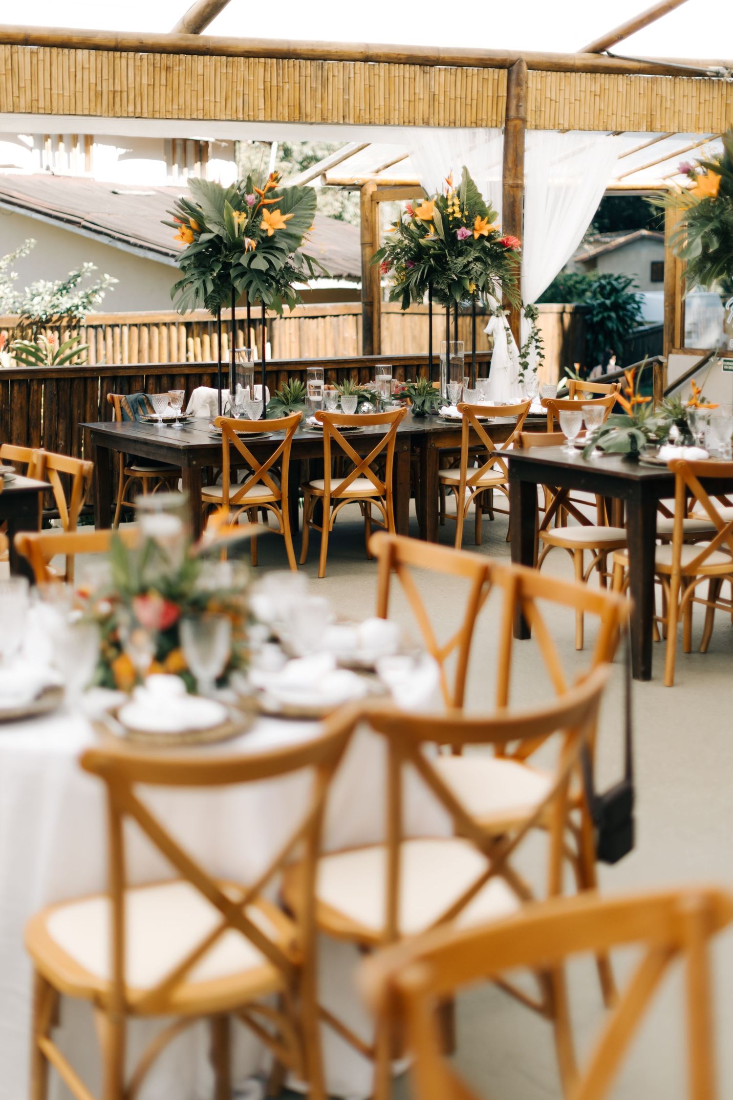 Reception venue with wooden crossback chairs and floral arrangements set up for a wedding.