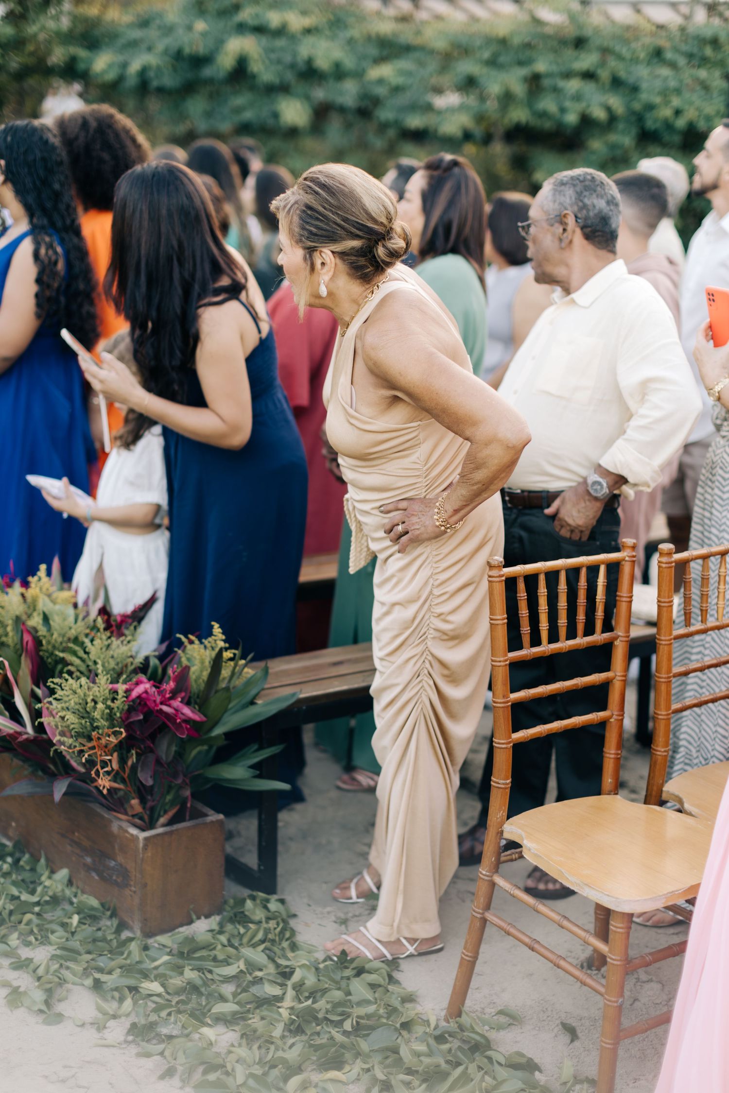 Guests stand beside wooden chairs at outdoor ceremony with tropical decorations.