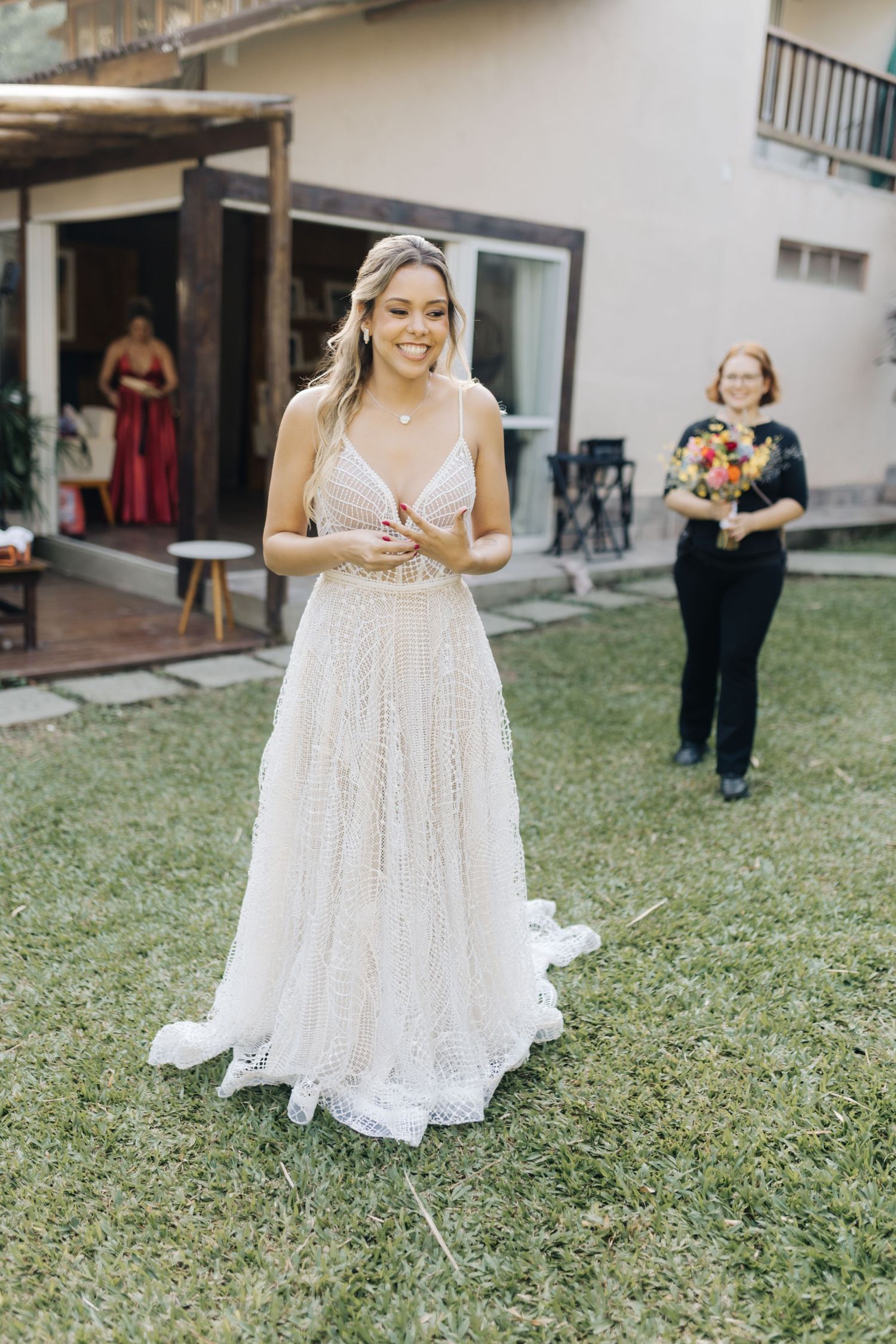 A person in a white wedding dress smiles while standing on a grassy lawn.