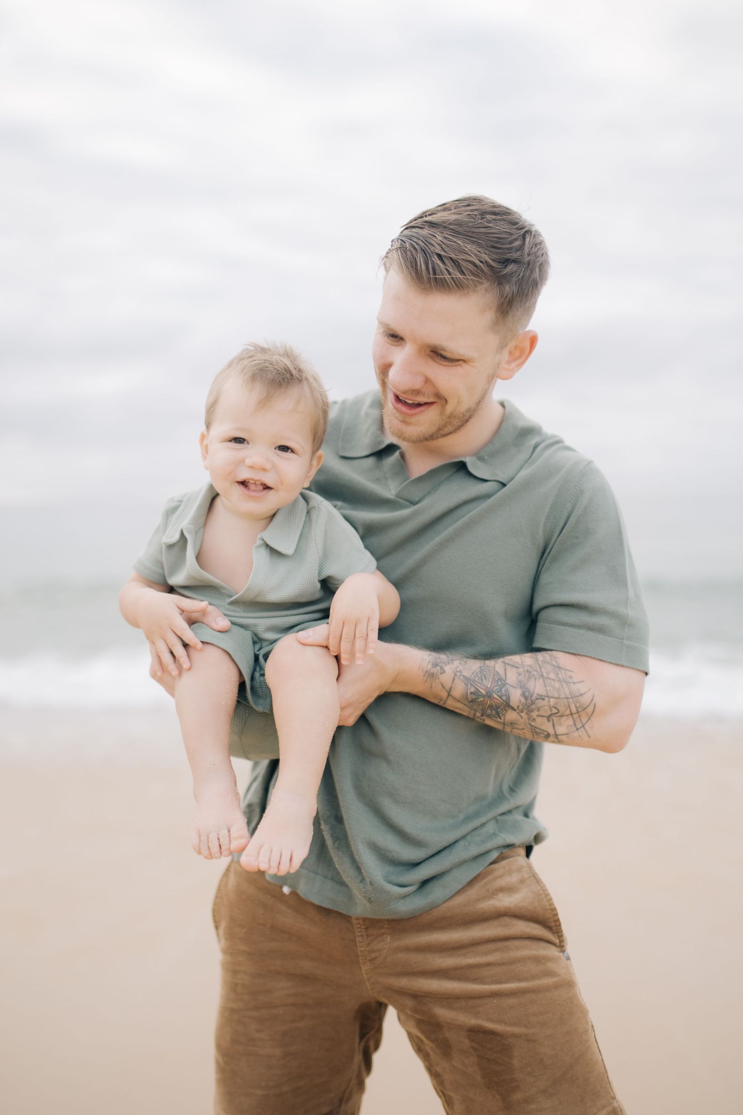 A parent and child laugh together during a playful beach photoshoot.