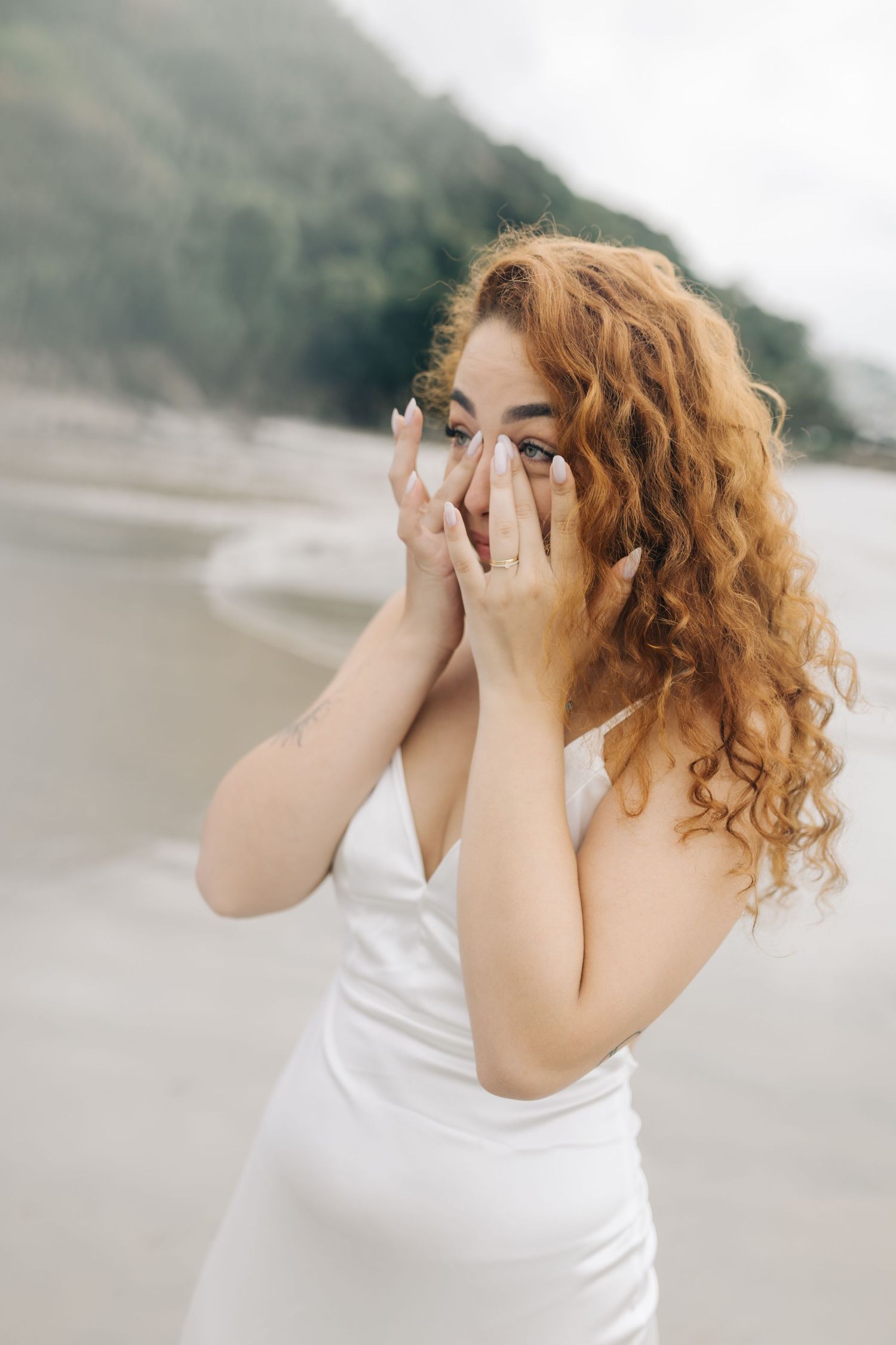 Woman in white dress showing emotional reaction during beach surprise moment.