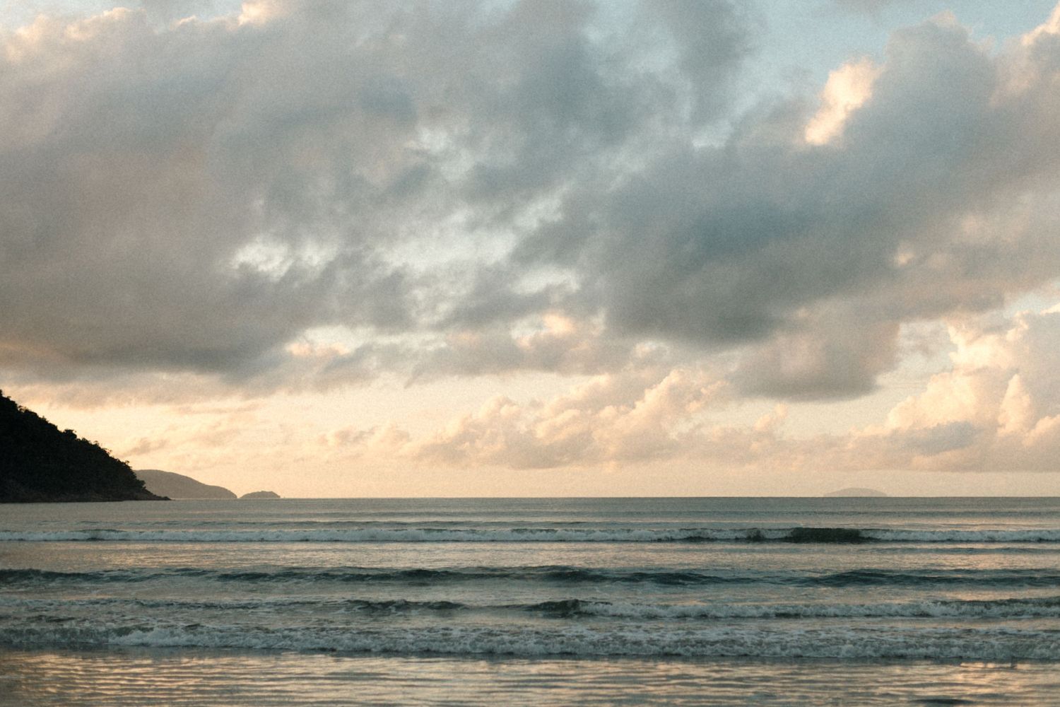 Dramatic sunset over ocean with cloudy sky and mountainous coastline.