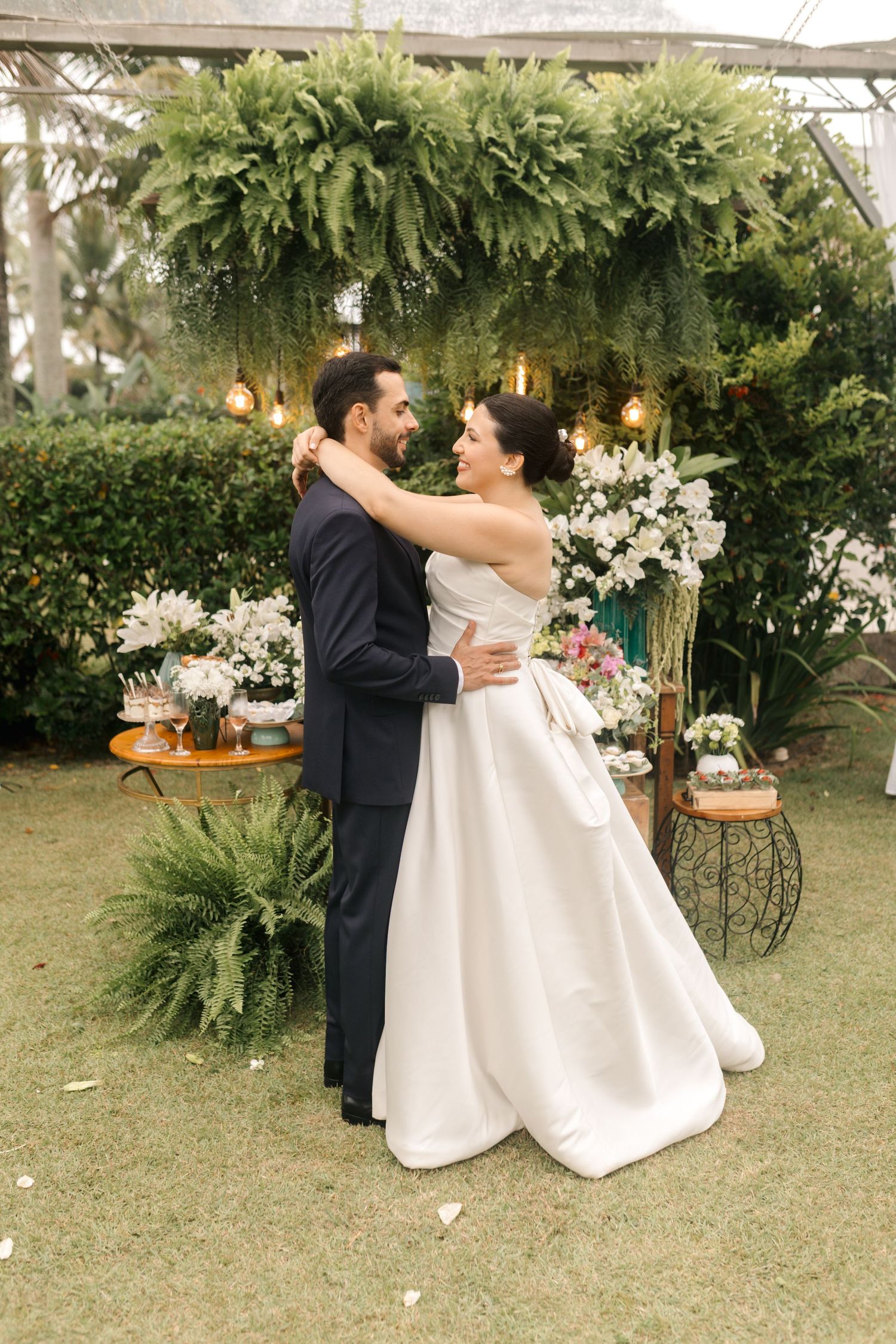 A couple dancing together in an outdoor garden setting surrounded by white flowers and greenery.