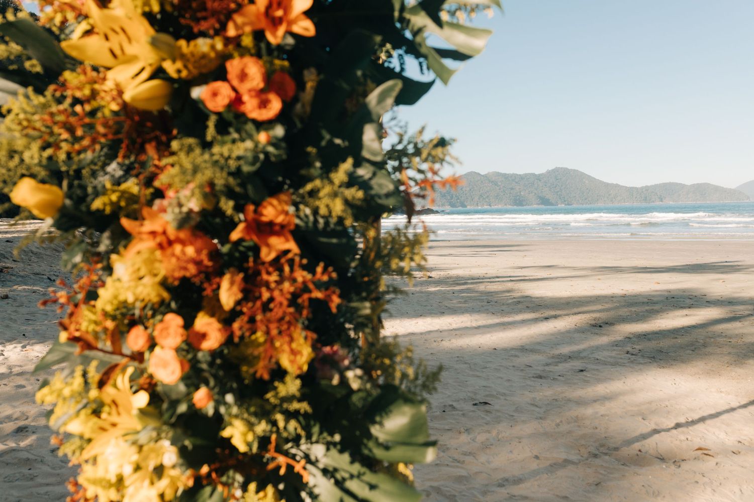 Vibrant orange and yellow floral arrangement framing a beach view.