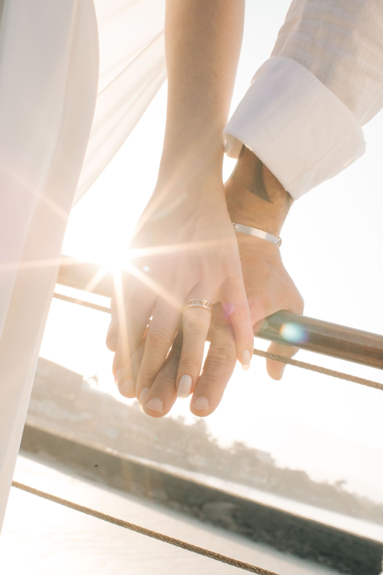 Close-up of newlyweds holding hands with sunlight streaming through in the background.