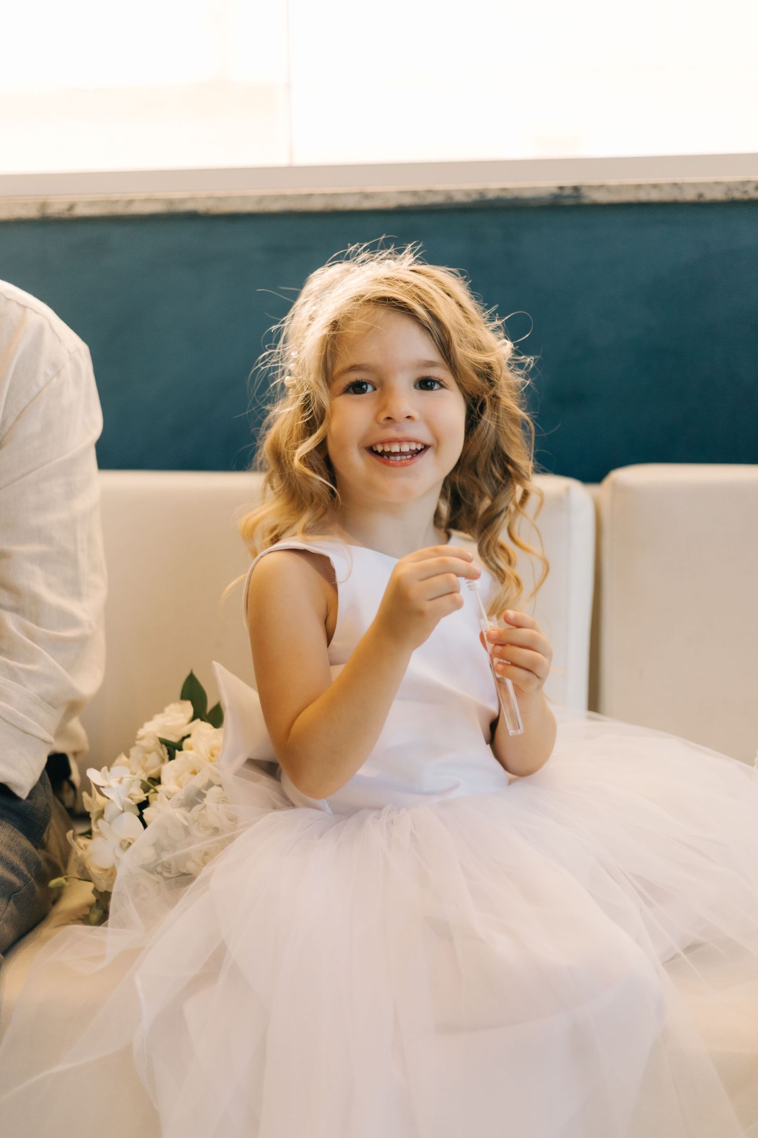 Young attendant in white tulle dress smiling joyfully during a special occasion.