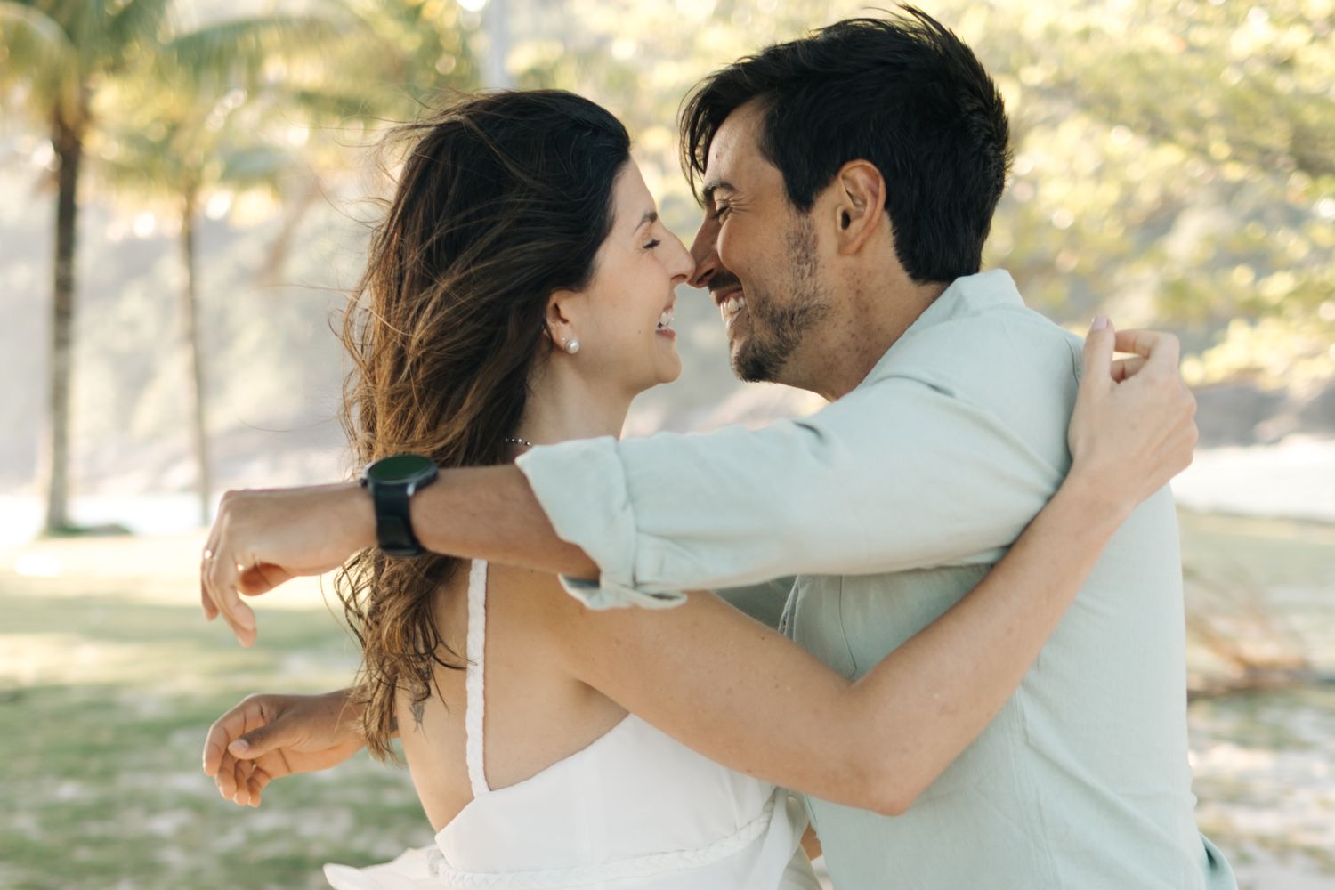 A couple embraces while dancing in a sunlit outdoor setting with trees in the background.