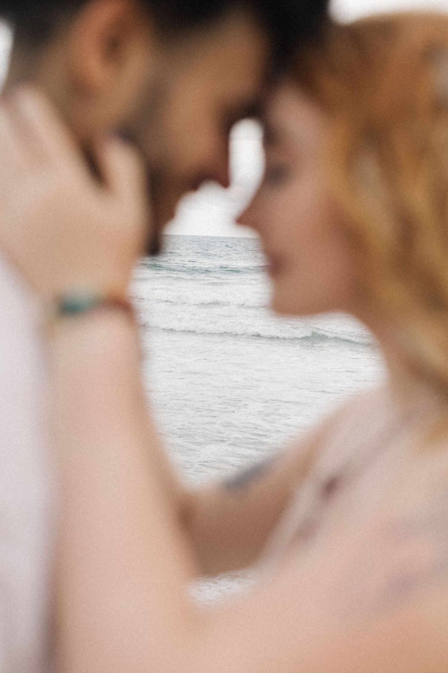 An artistic close-up shot of a couple embracing with the ocean visible in the background.