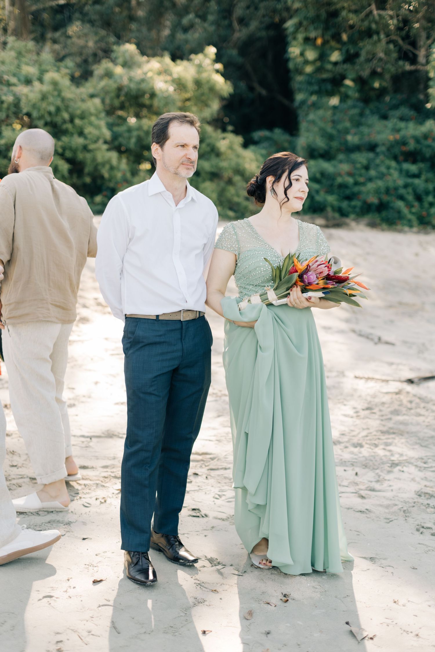 Wedding guests in formal attire walking along a scenic beach path.