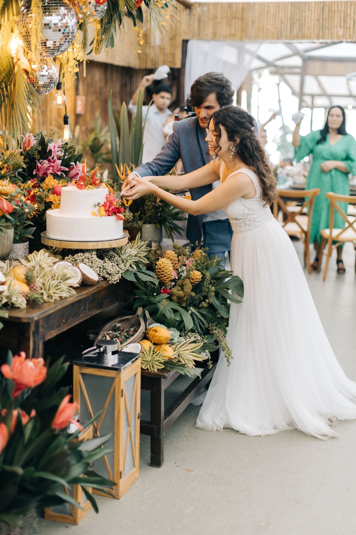 Couple cuts their wedding cake surrounded by tropical flowers and decorative elements.
