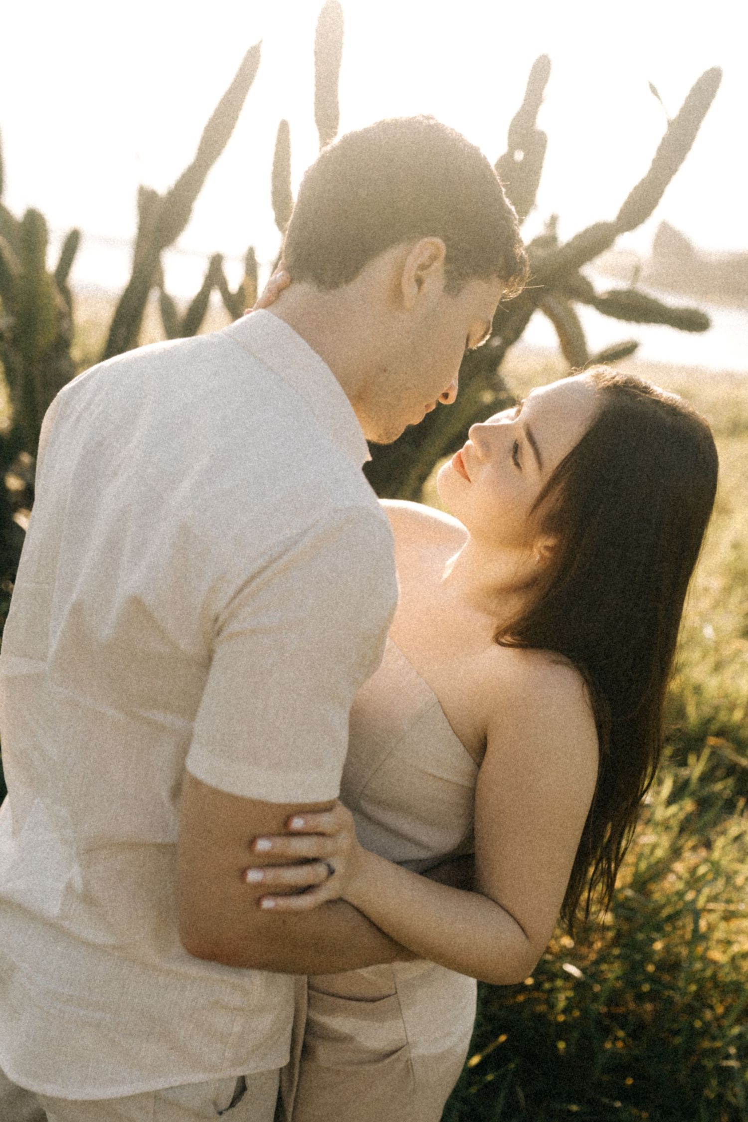 A couple in white clothing shares romantic moments in golden sunlight.