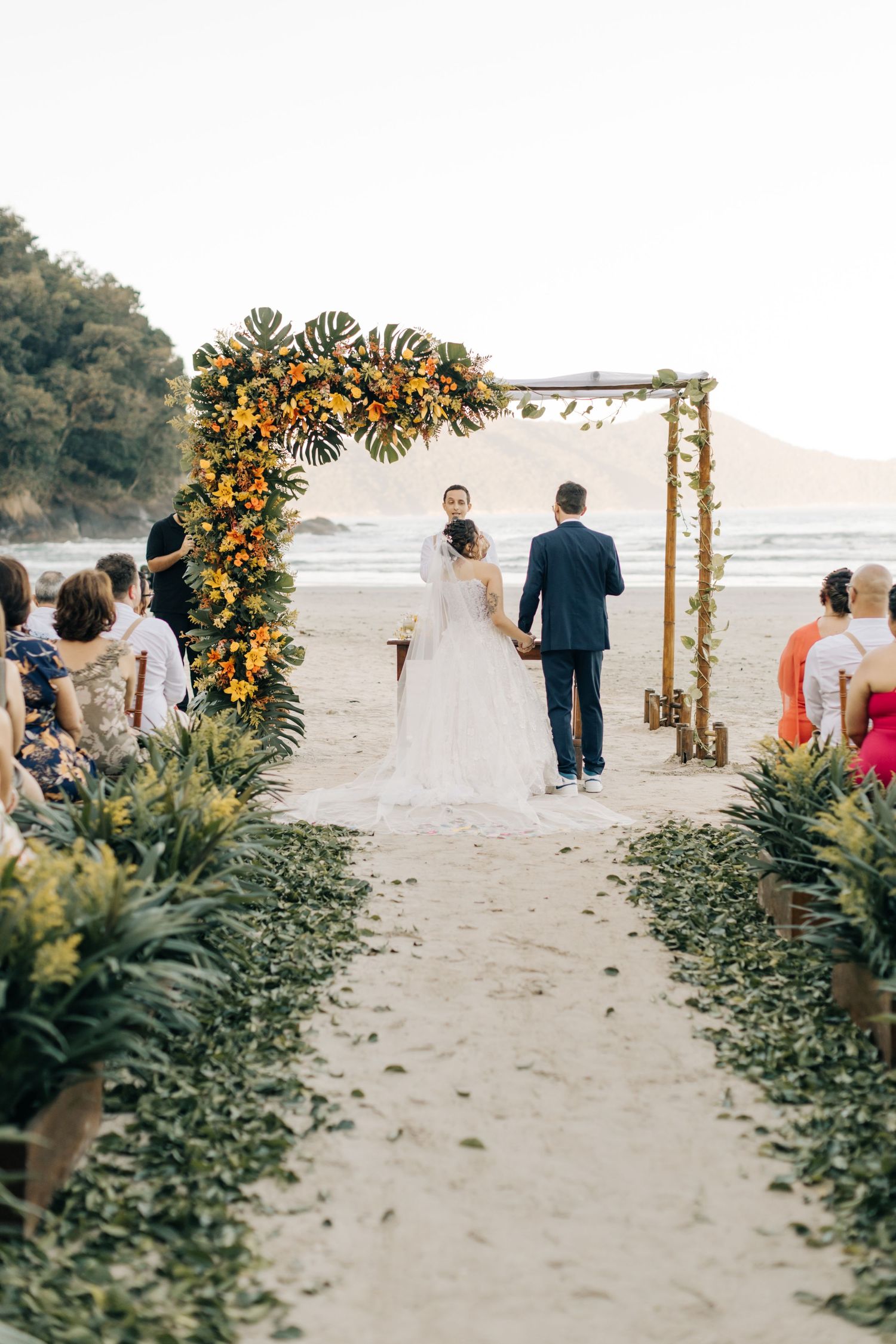 Beautiful beach wedding ceremony setup with floral arch decorated in yellow and orange blooms on a sandy shore.