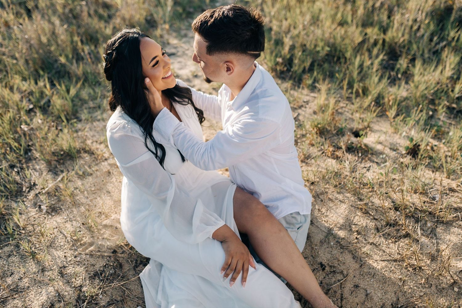 Candid shots of couple playfully interacting on sandy beach in white attire.