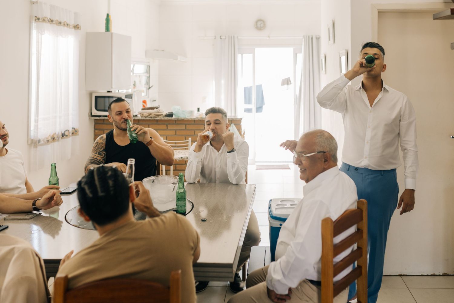 Friends gathered around table enjoying drinks and conversation in bright room.
