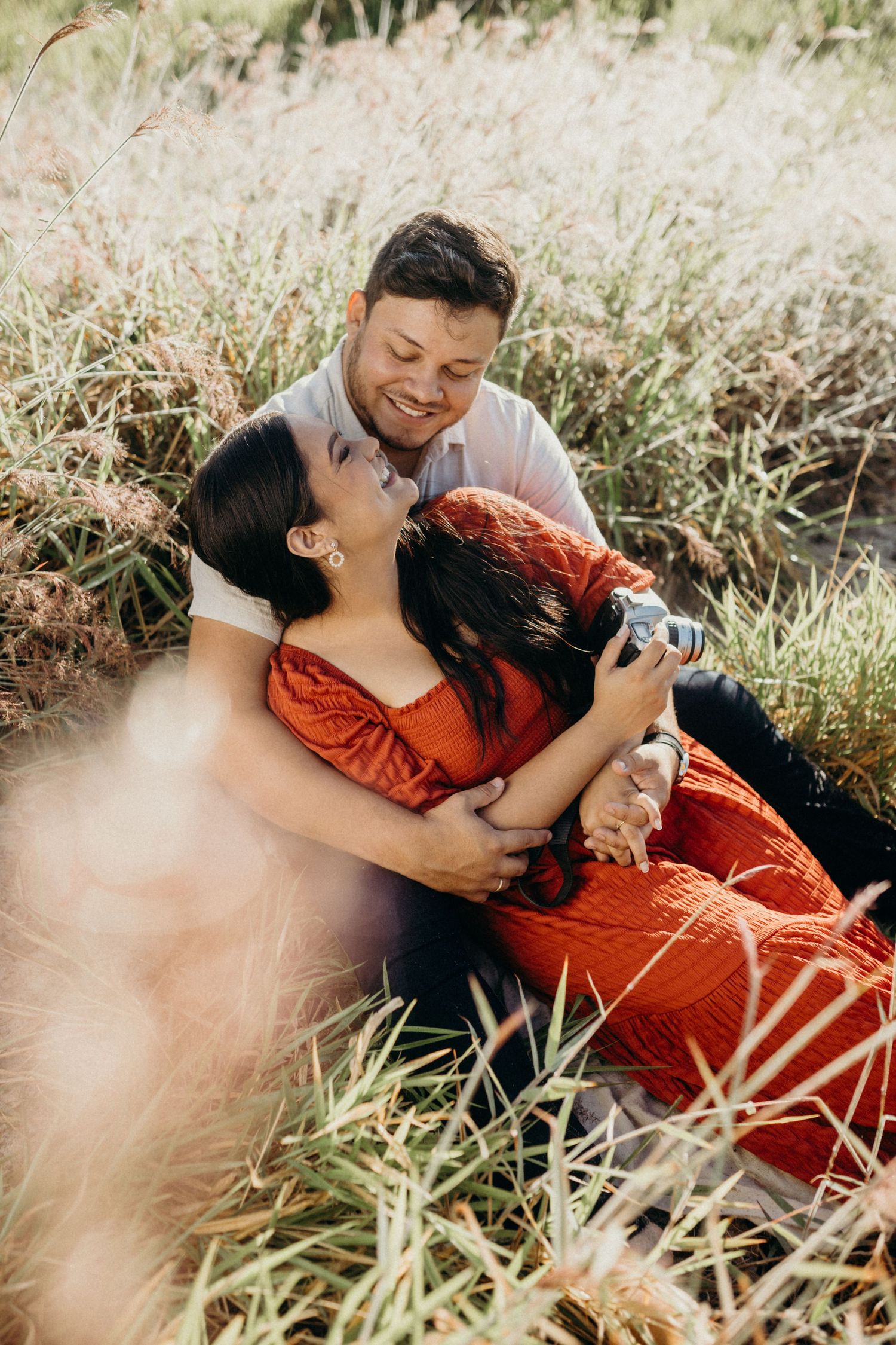 An intimate portrait of a couple laughing together while holding a camera in a grassy field.