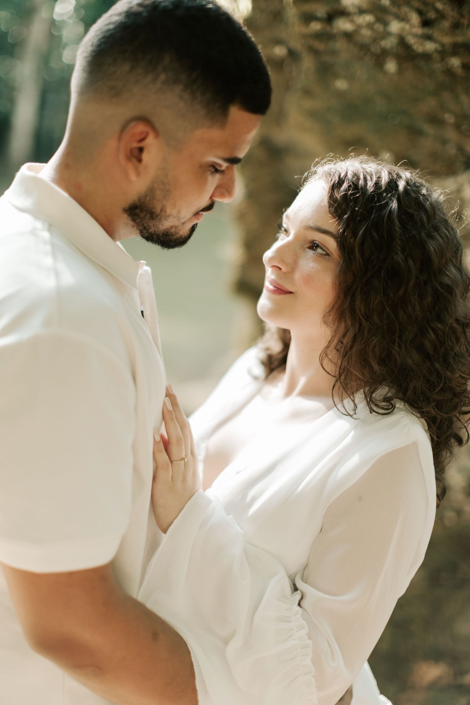 A couple in matching white outfits shares an intimate moment against a natural backdrop.