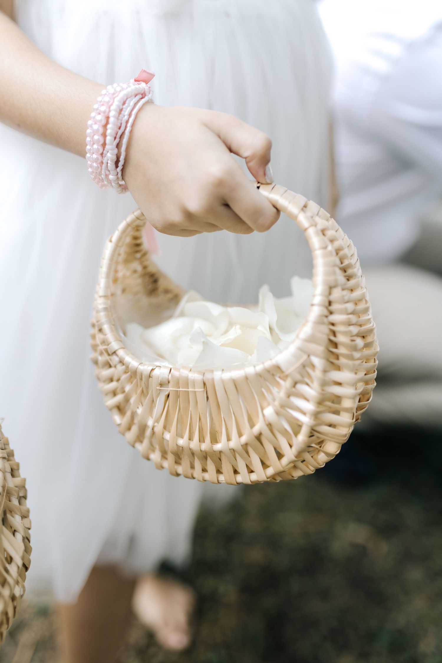 A delicate wicker basket held by hands wearing pink bracelets against a white dress.