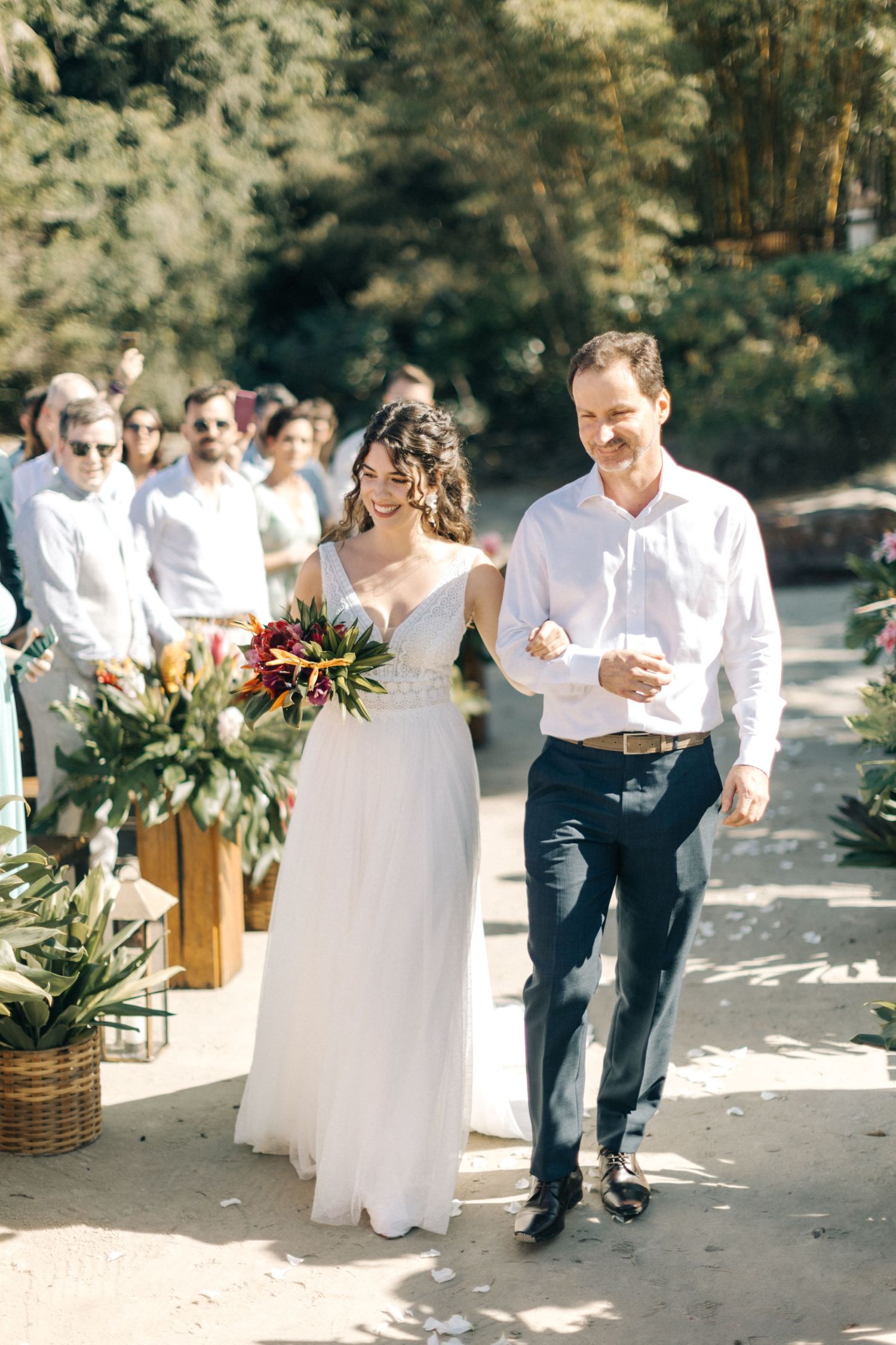 Sunlit outdoor wedding ceremony with tropical floral decorations lining the aisle.