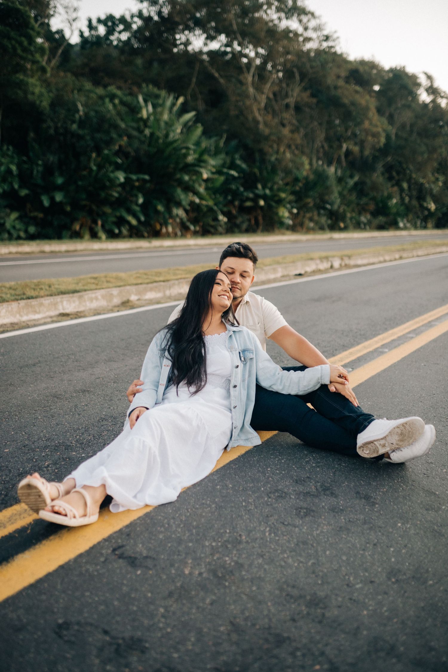 Couple laying on the yellow lines of an empty road during a photoshoot.