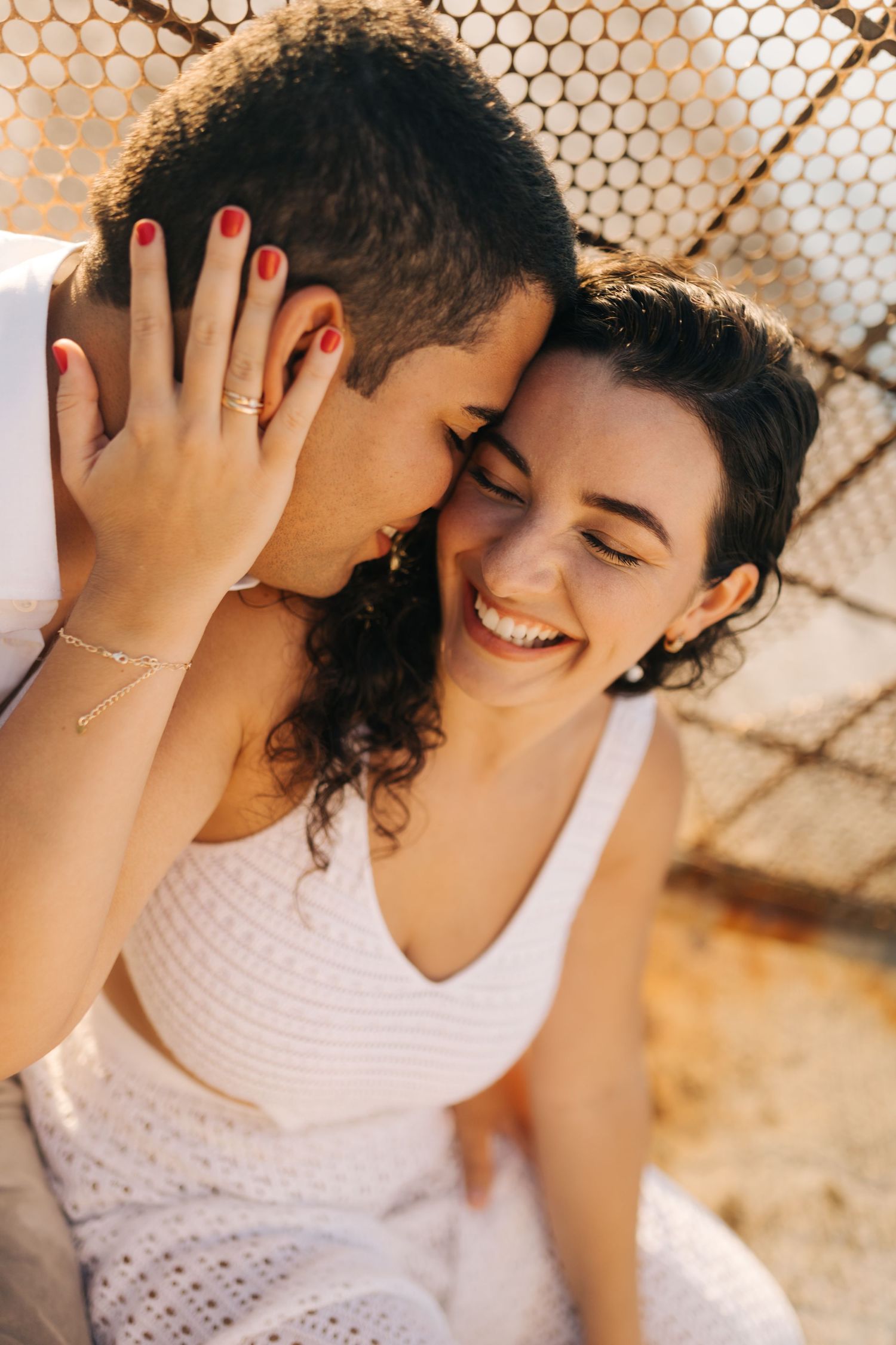 Intimate portrait of a couple embracing and laughing against a honeycomb patterned backdrop.