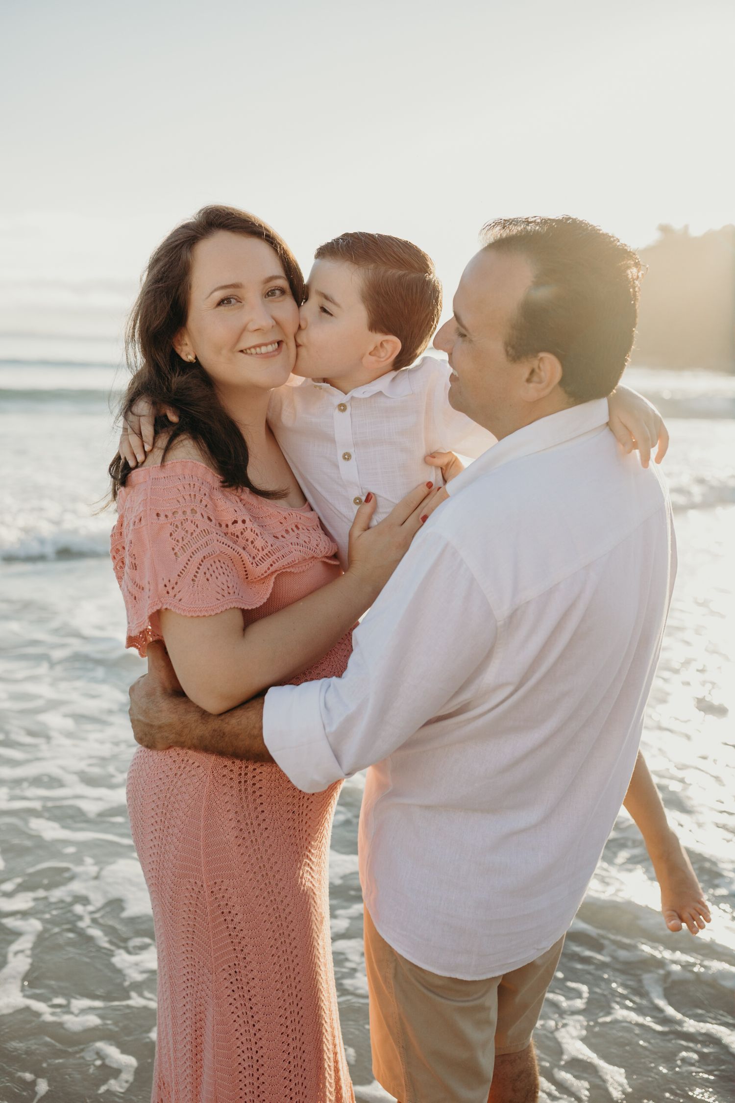 A tender family moment captured on the beach at sunset wearing coordinated outfits in coral and white.