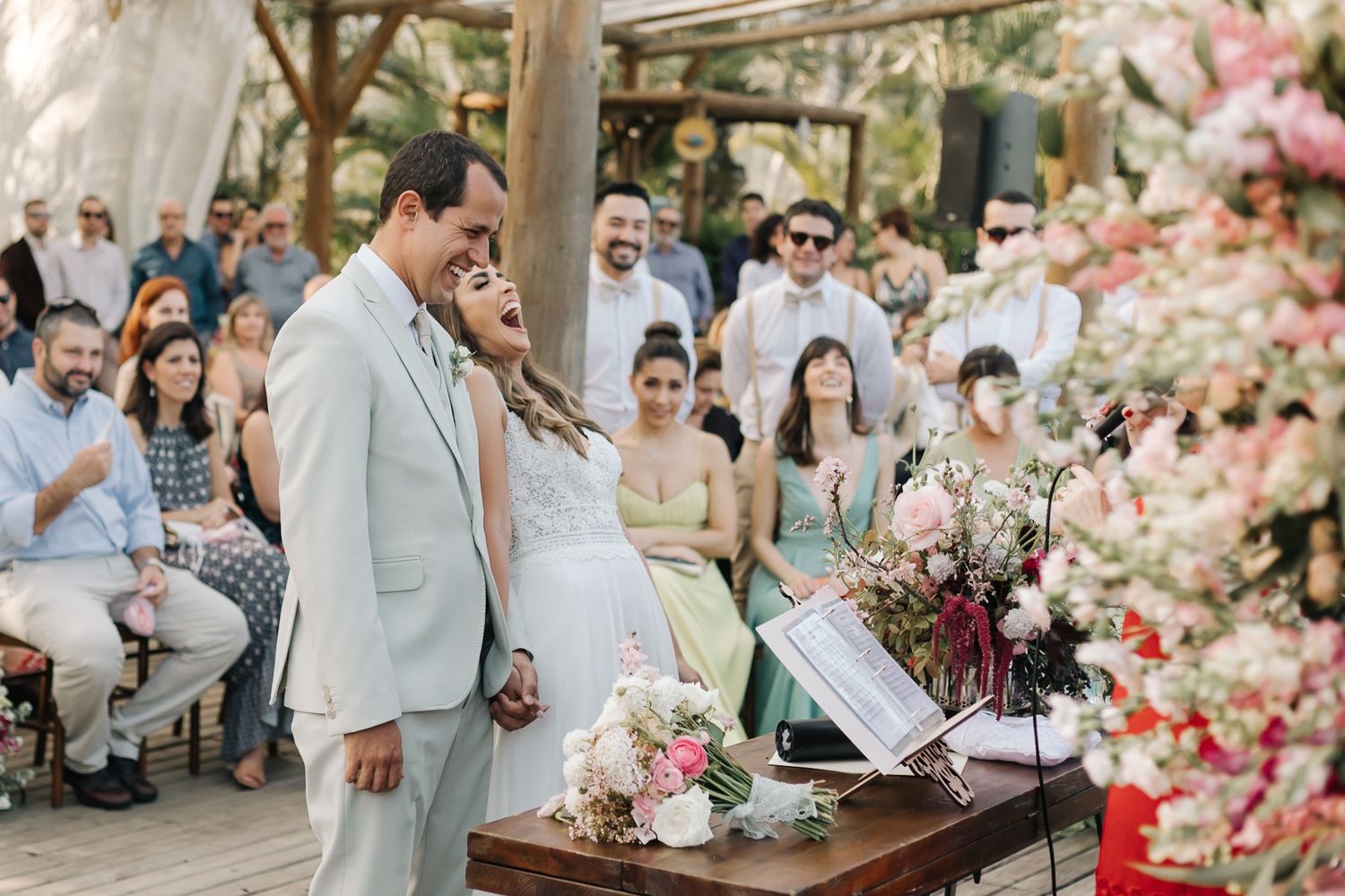 Outdoor wedding ceremony with pink floral decorations under a wooden canopy.