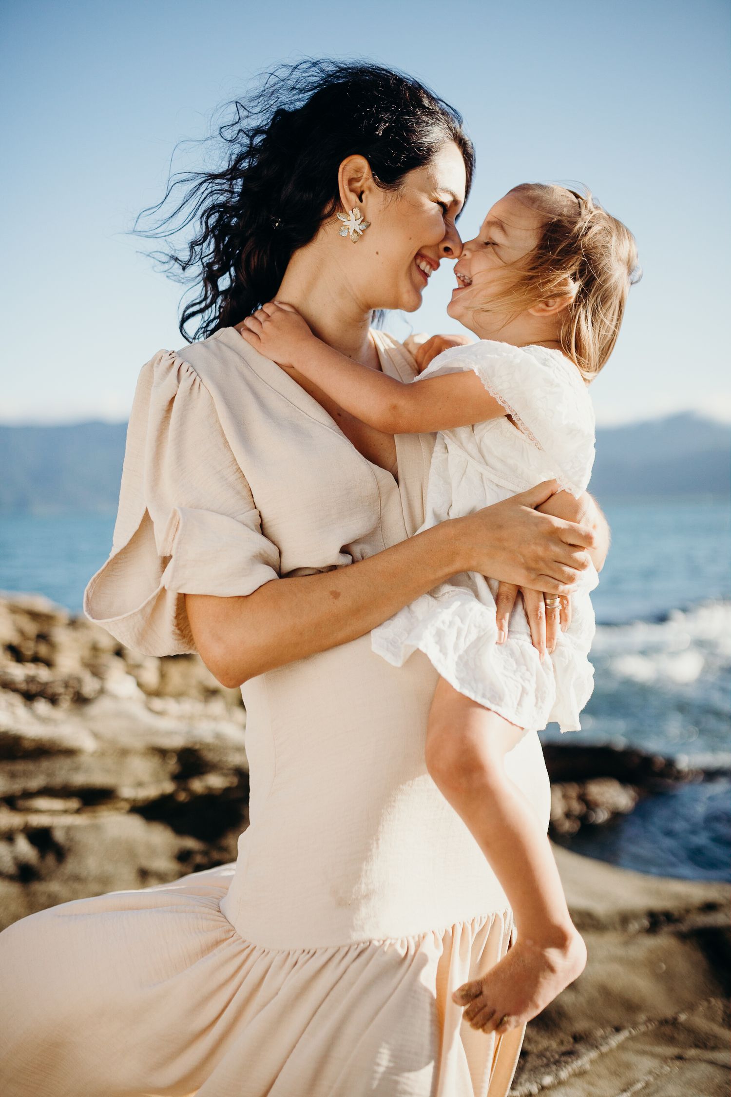 Intimate portrait of parent and child laughing together against ocean backdrop.