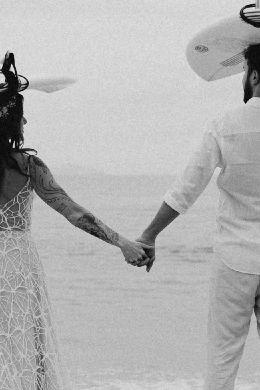 Black and white photo of a couple holding hands on a beach in wedding attire.