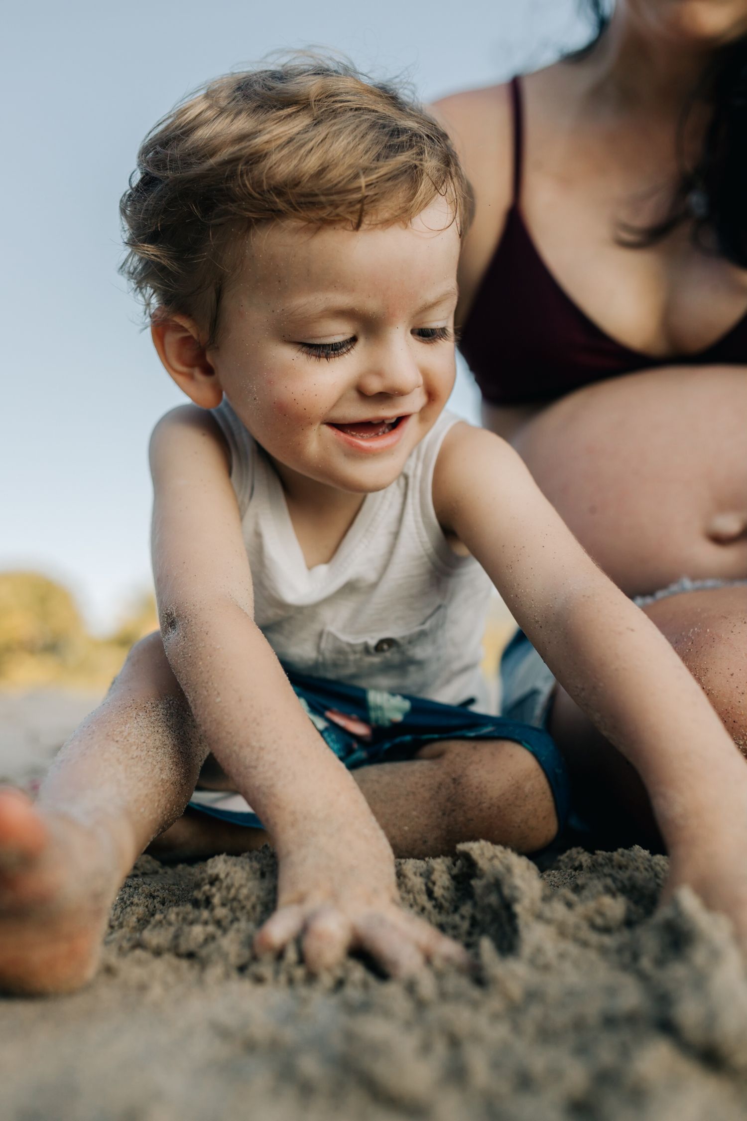 Close-up view of small hands digging and exploring in beach sand with joyful expression.
