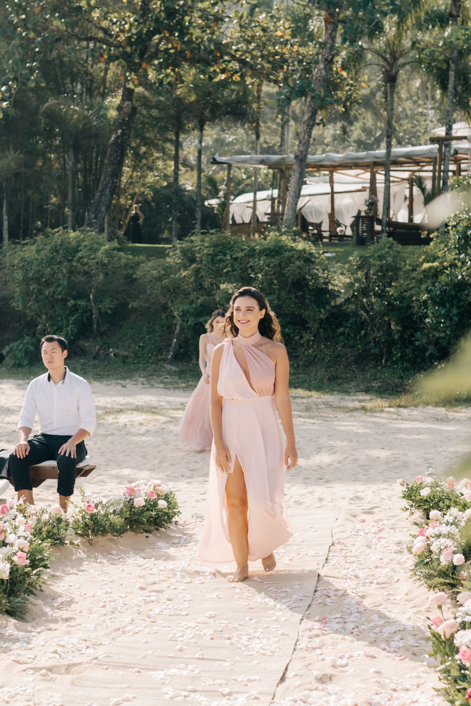 A person in a flowing pink dress walks down a garden path lined with roses.