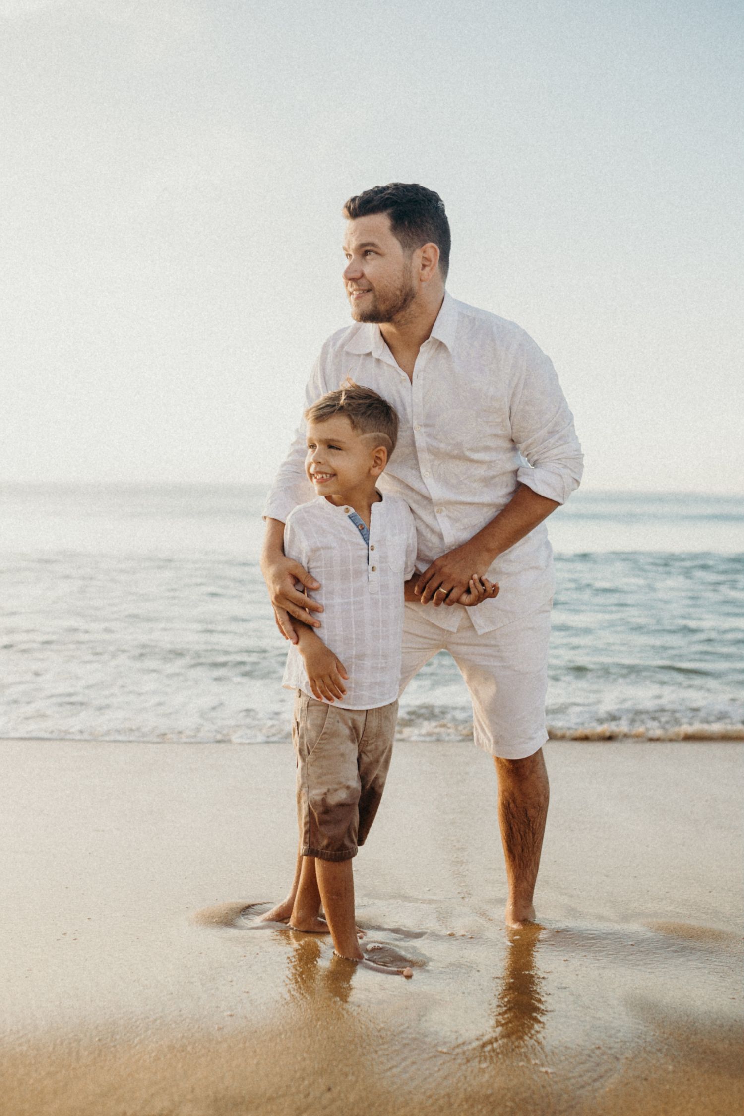 Parent and child sharing a tender moment while standing on beach at sunset.
