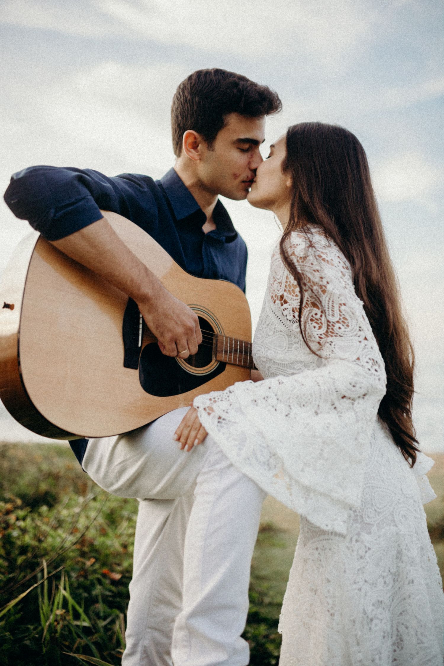 A romantic moment between a couple with an acoustic guitar on a scenic hillside.