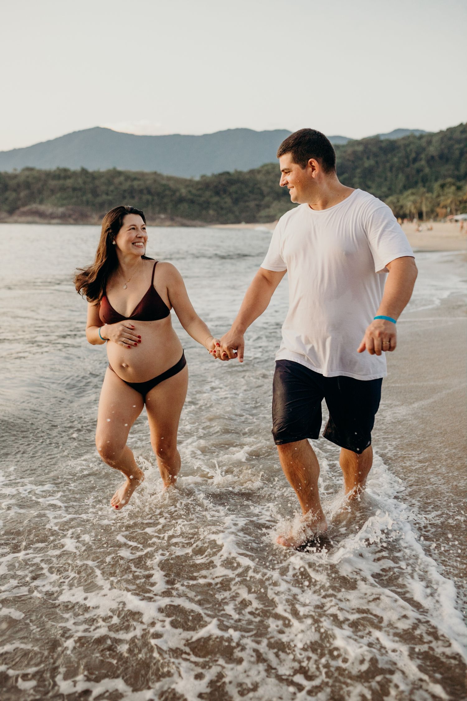 Happy couple holding hands while playing in the ocean waves at sunset.