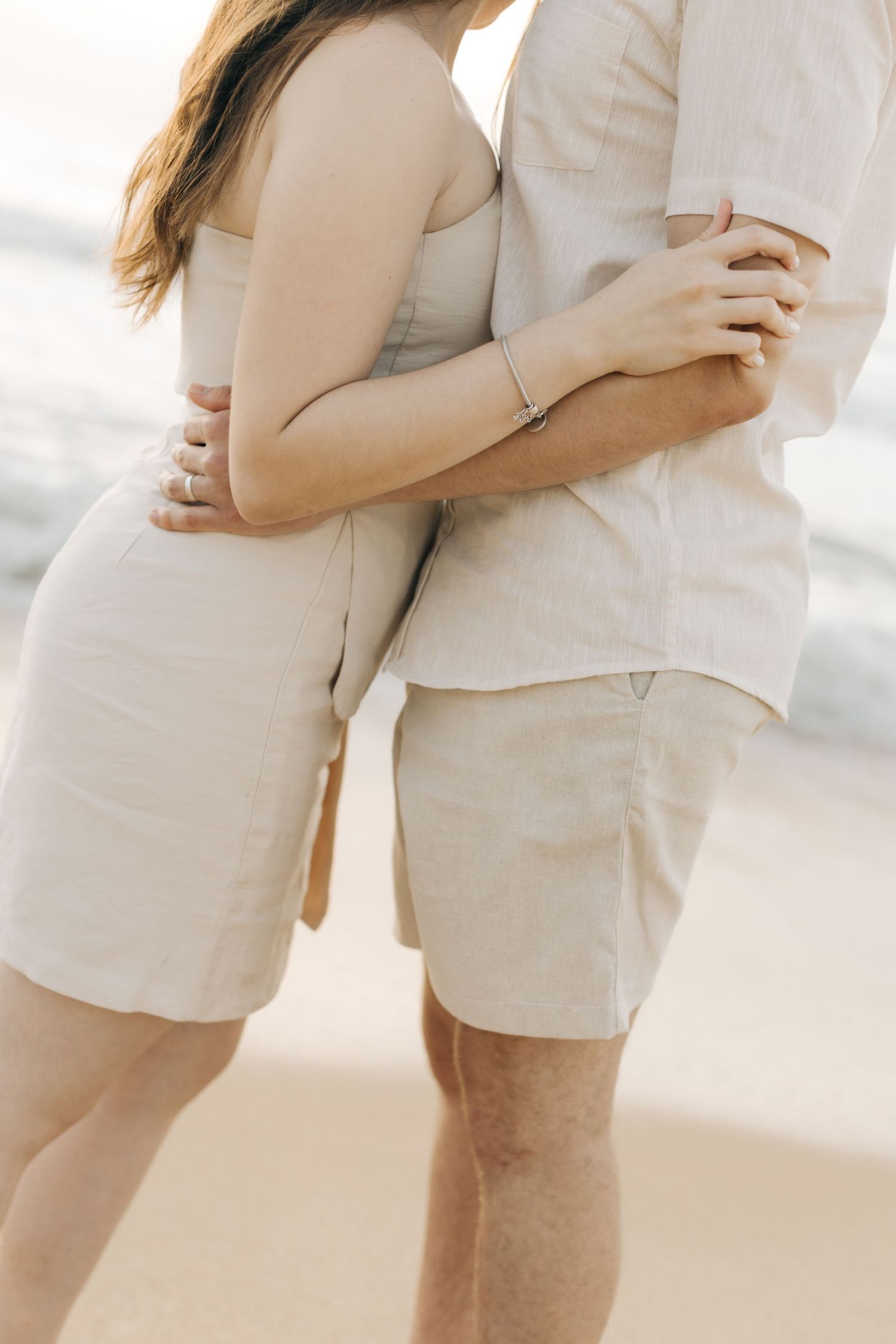 Close-up detail shot of a couple embracing in coordinated neutral colored beachwear.