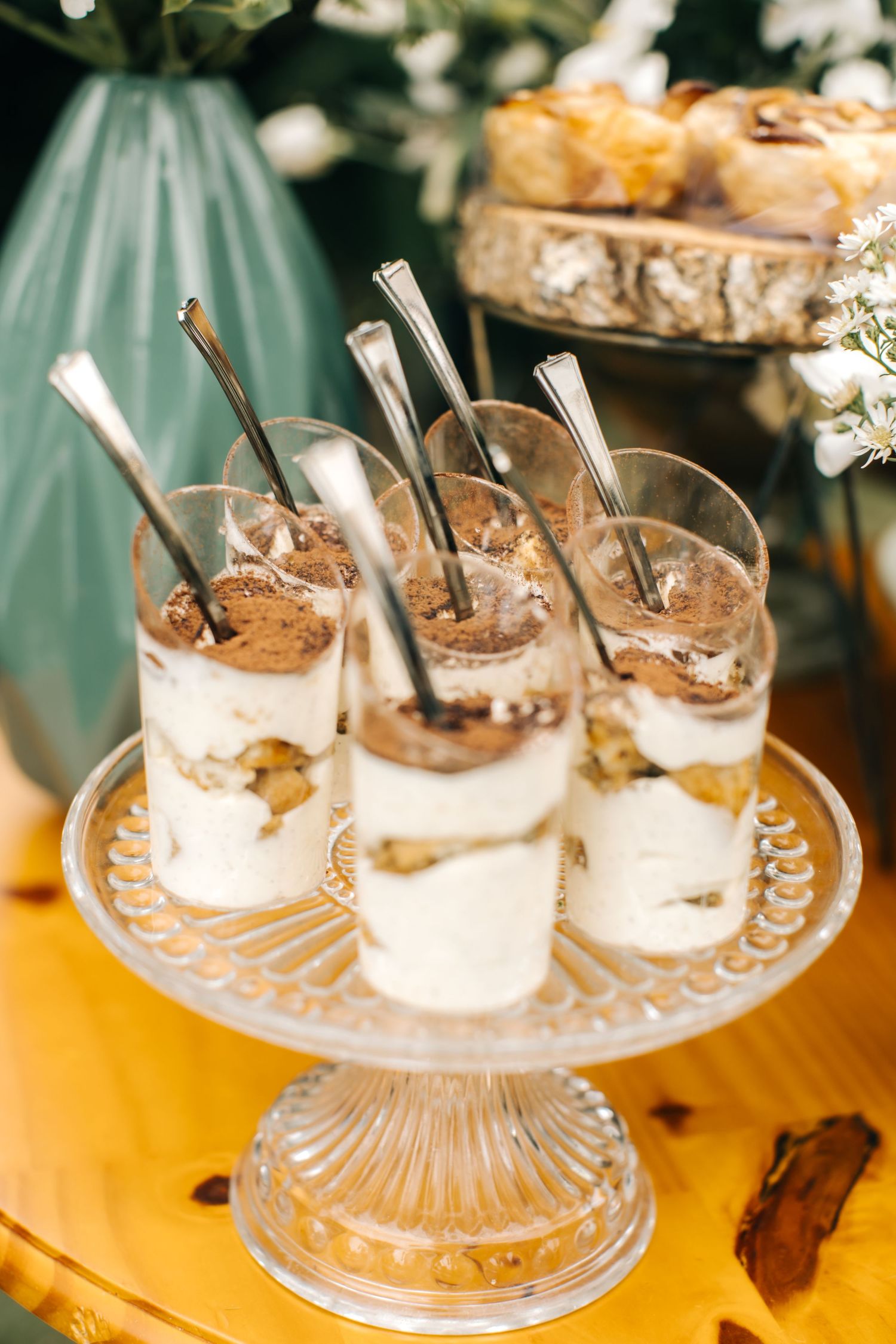 Individual dessert parfaits arranged on a crystal cake stand with silver spoons.