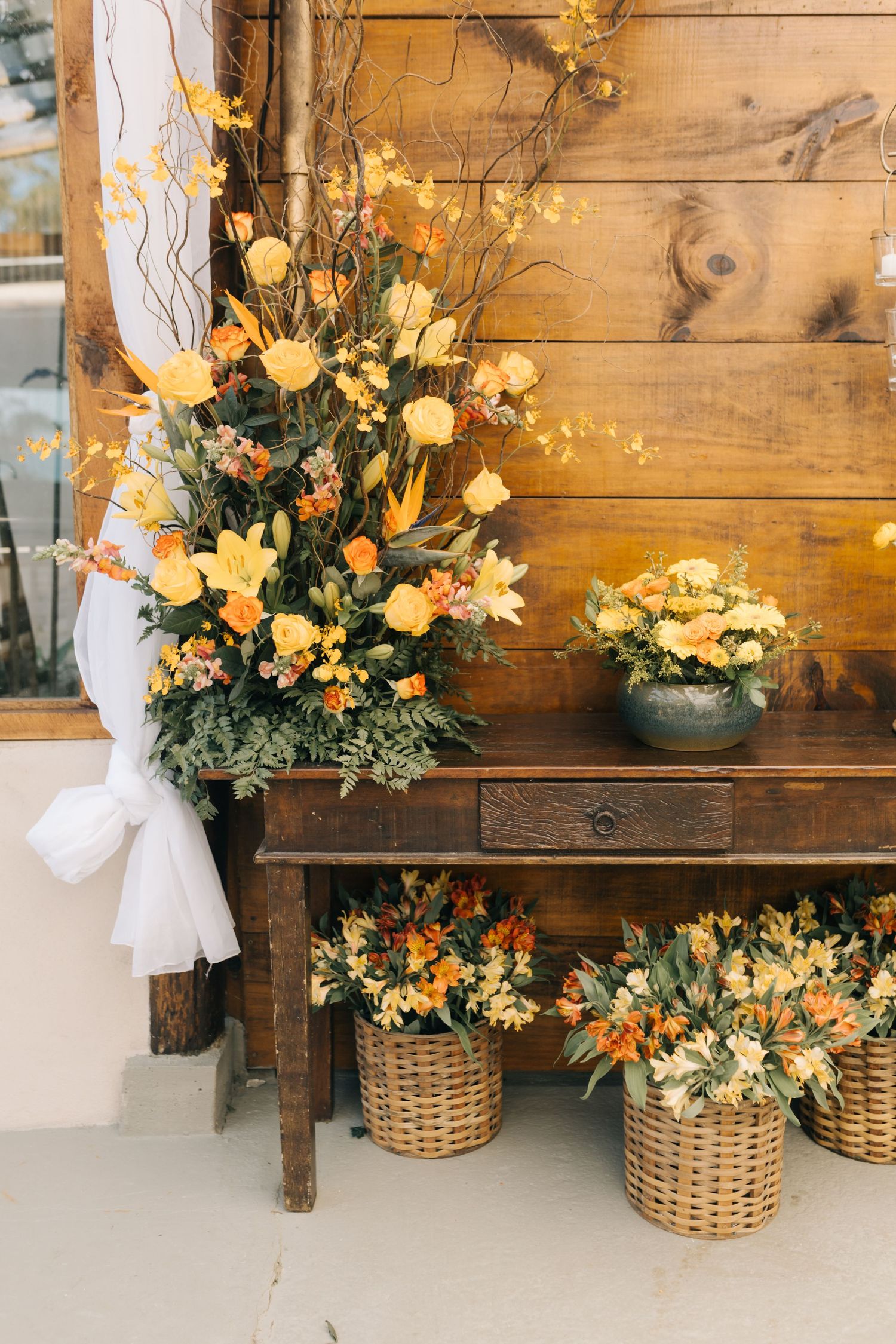 Rustic wooden bench decorated with yellow floral arrangements in wicker baskets.