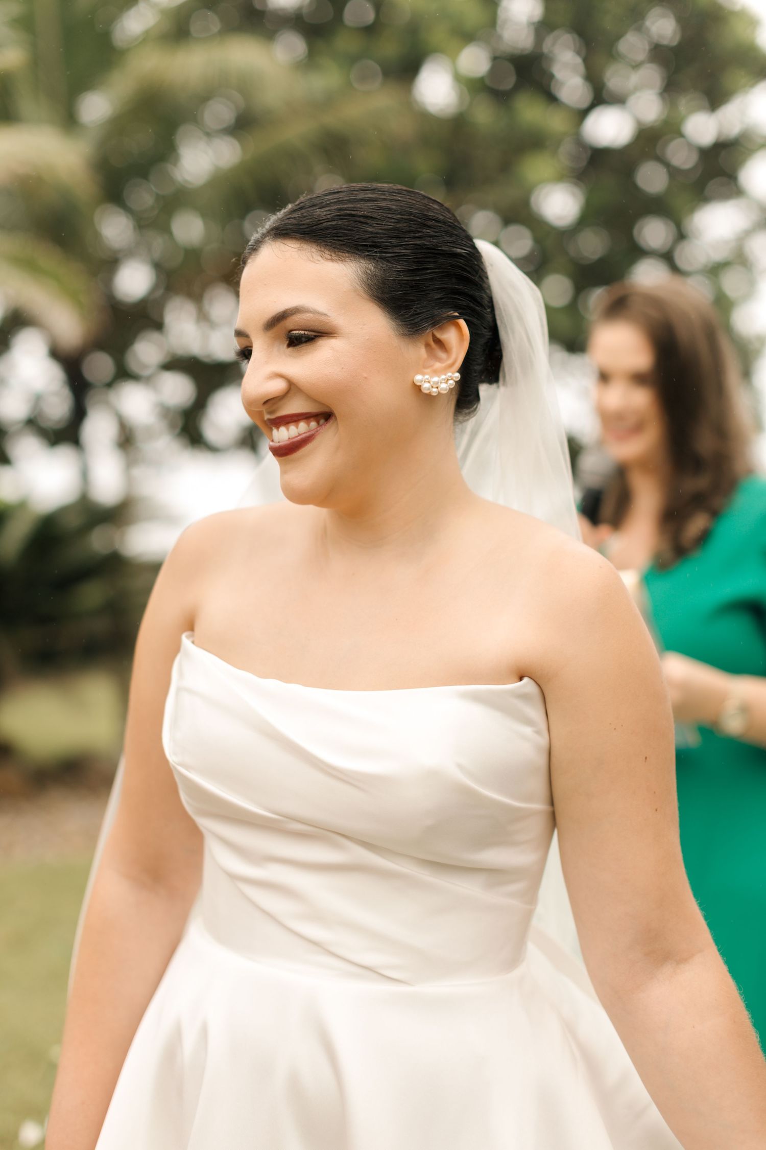A radiant bride in a strapless white gown smiling during her outdoor wedding ceremony.