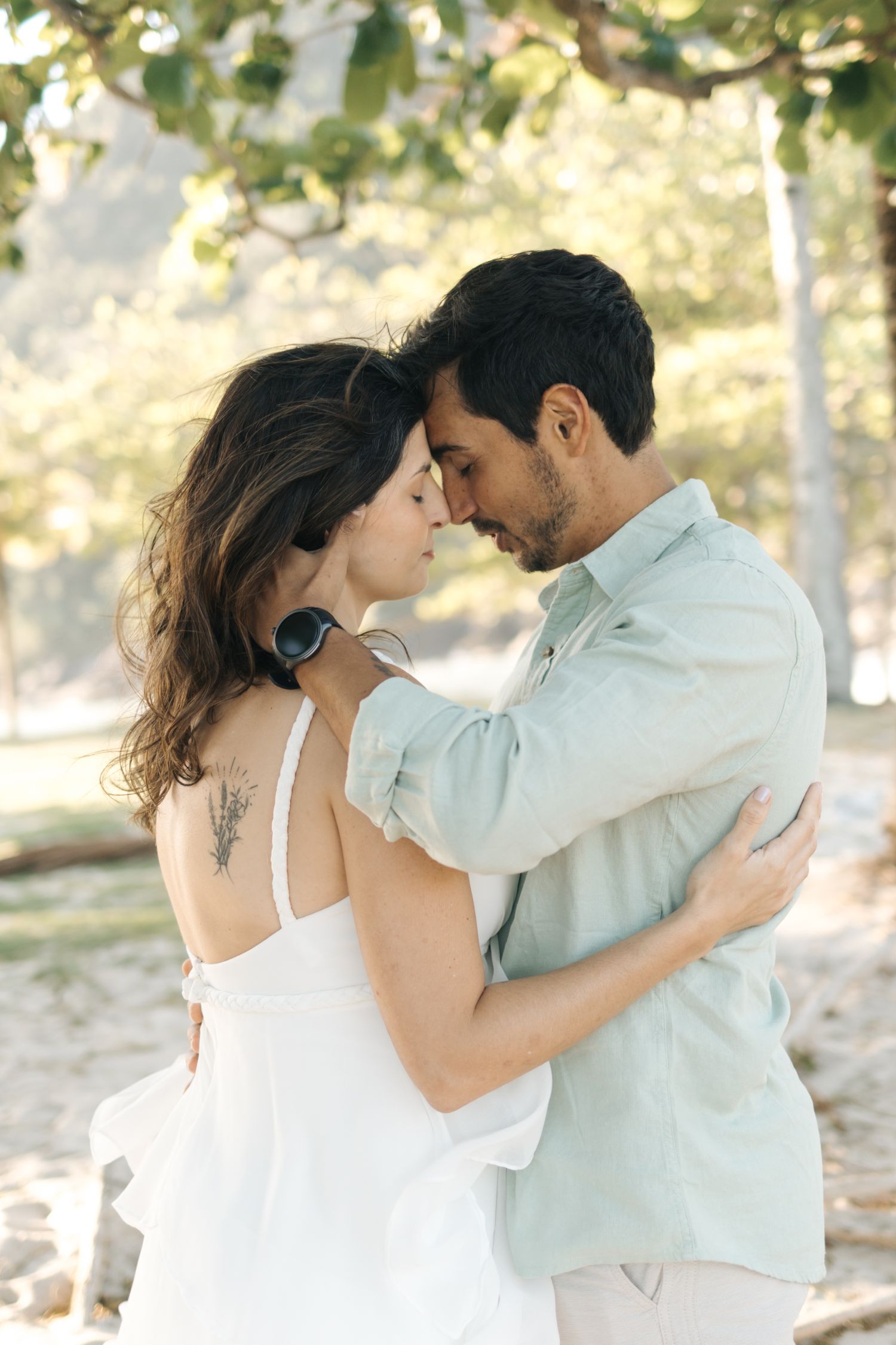 Two people embrace while wearing coordinated white and mint outfits in a natural setting.