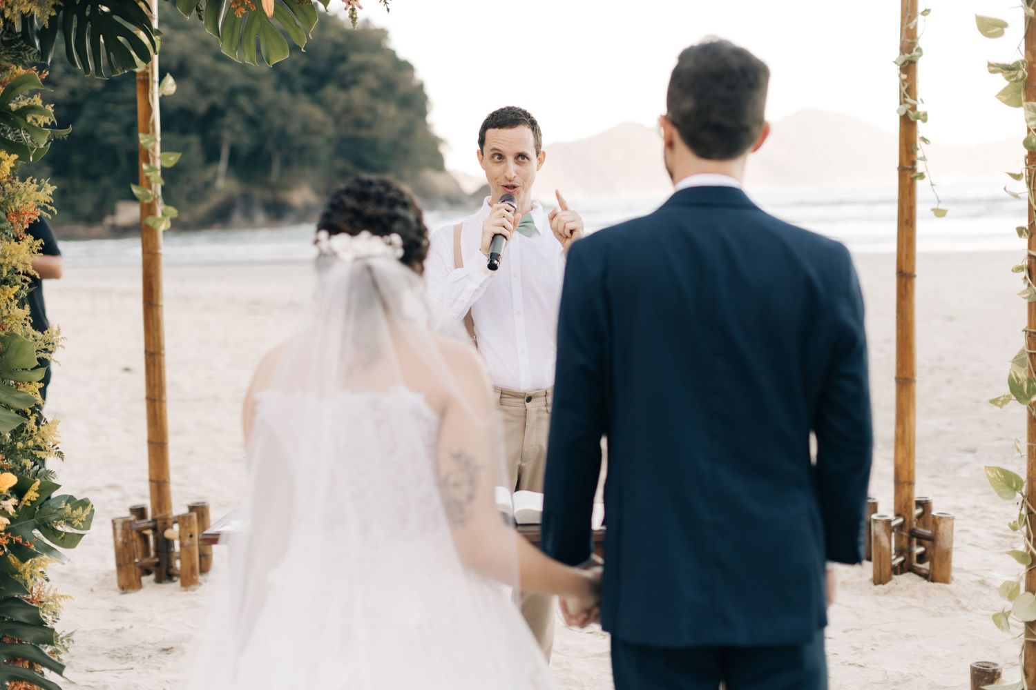 A beachside wedding ceremony with palm trees and decorative wooden pillars at sunset.