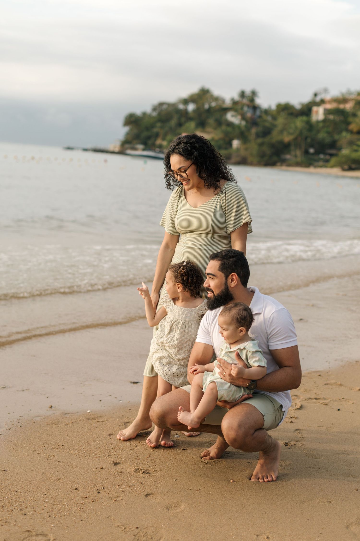 Family enjoying a tender moment together while crouching on a sandy beach at sunset.