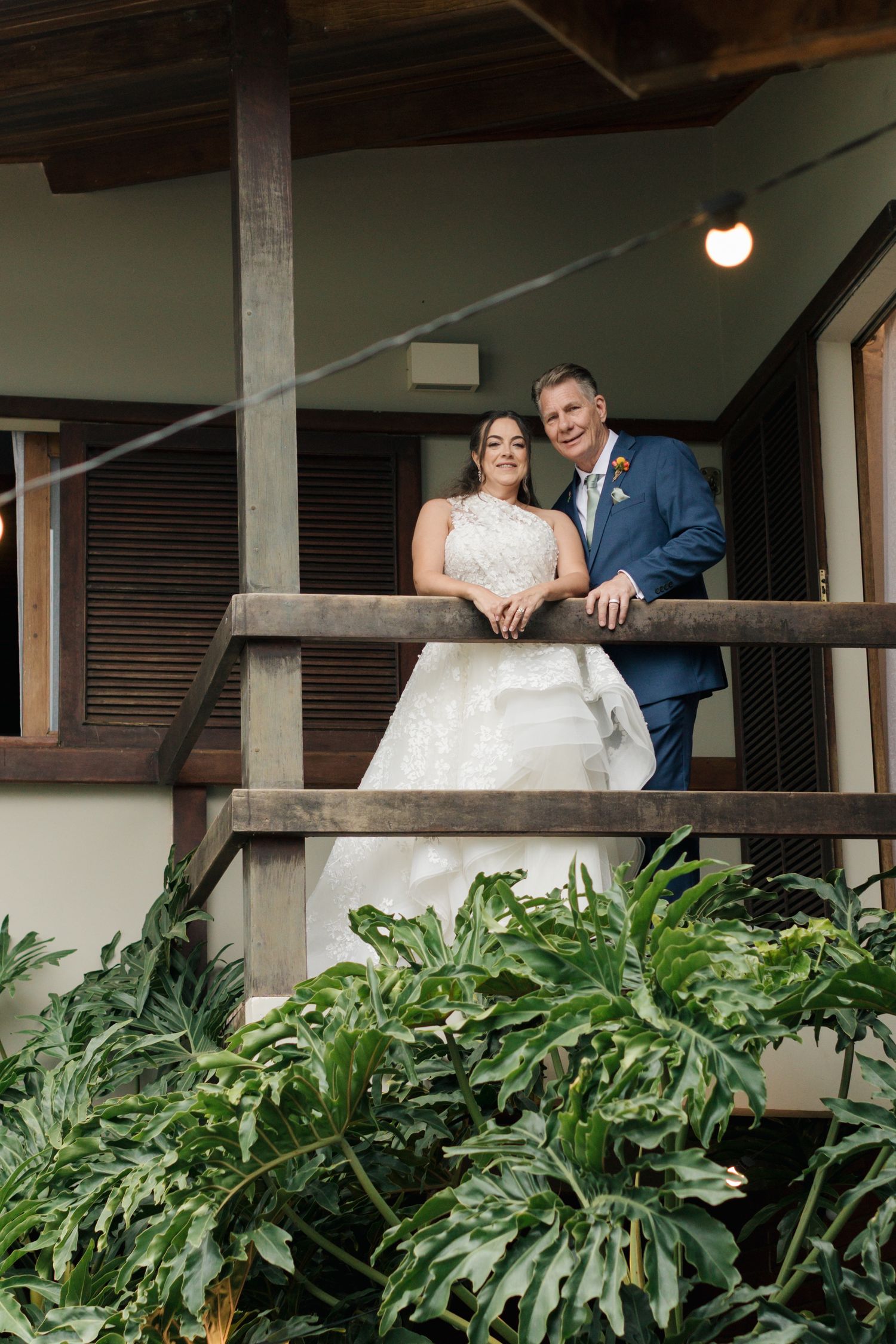 Wedding couple shares a moment on a covered porch surrounded by lush tropical plants.