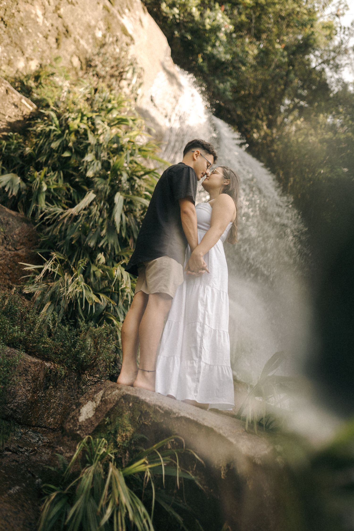 An artistic photoshoot sequence showing a couple's tender moments by a tropical waterfall.