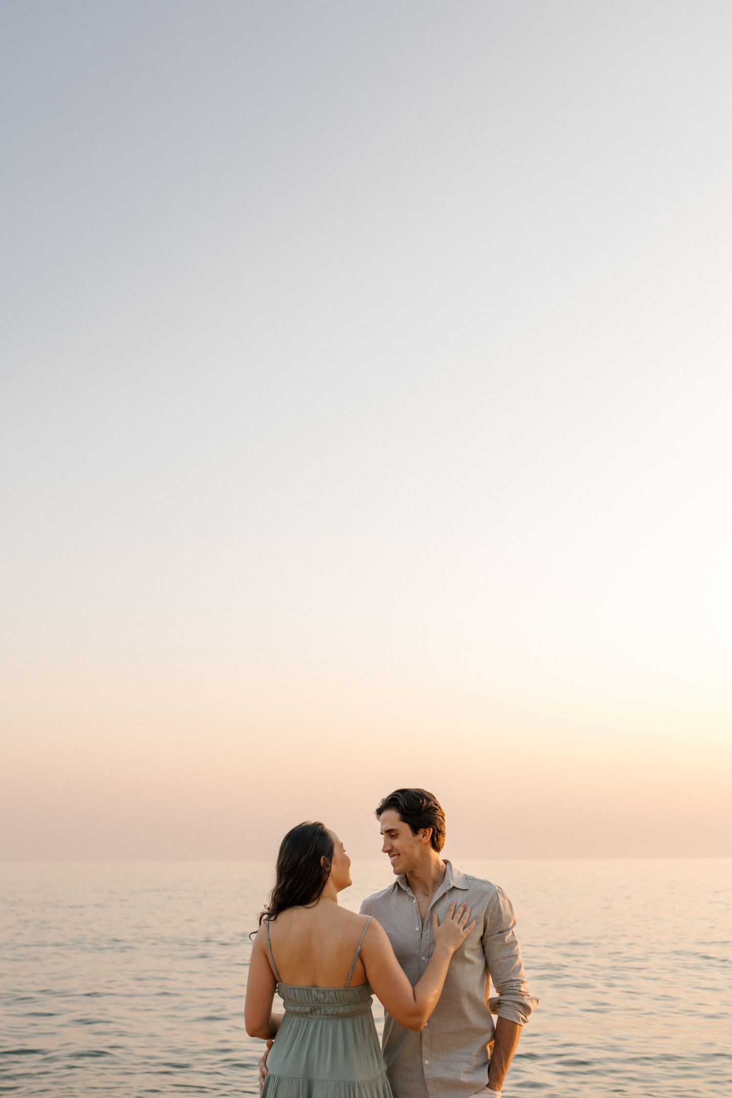 Romantic couple stands together at sunset by the calm ocean as warm light bathes the peaceful seascape.