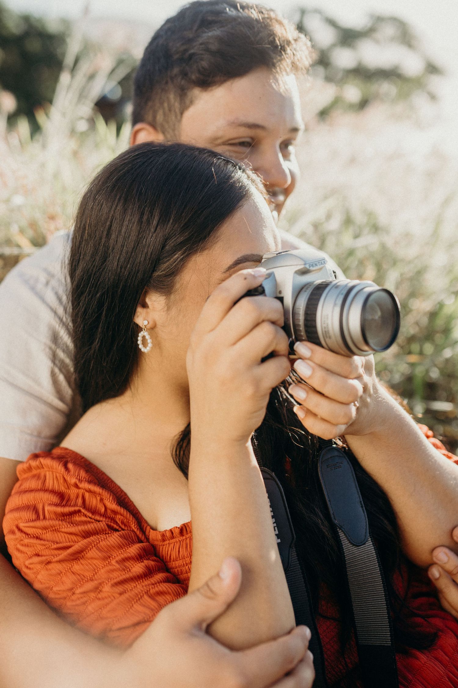 A couple shares an intimate moment while taking photos together in golden afternoon light.
